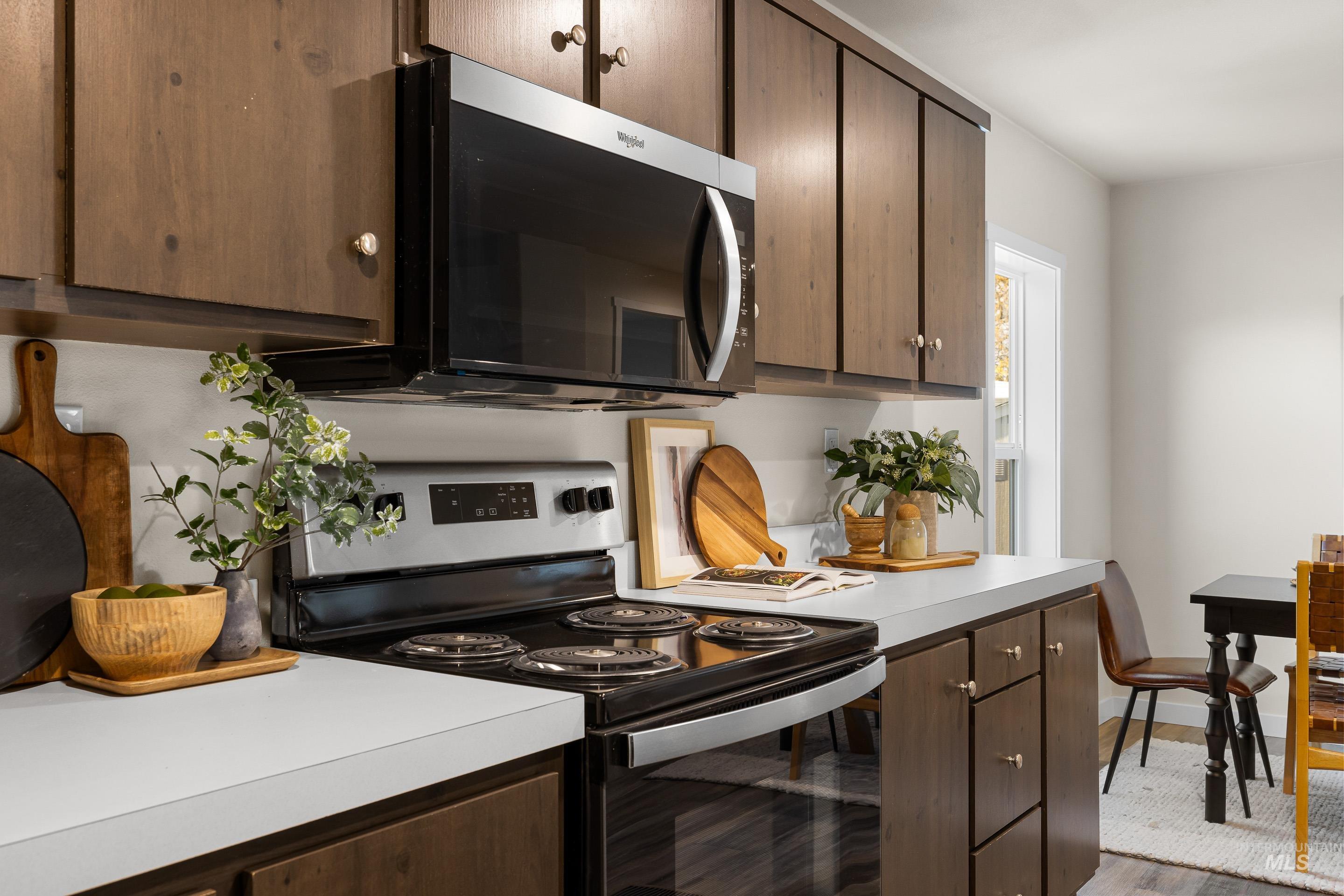 Kitchen featuring appliances with stainless steel finishes, dark brown cabinets, light countertops, and light wood-style floors