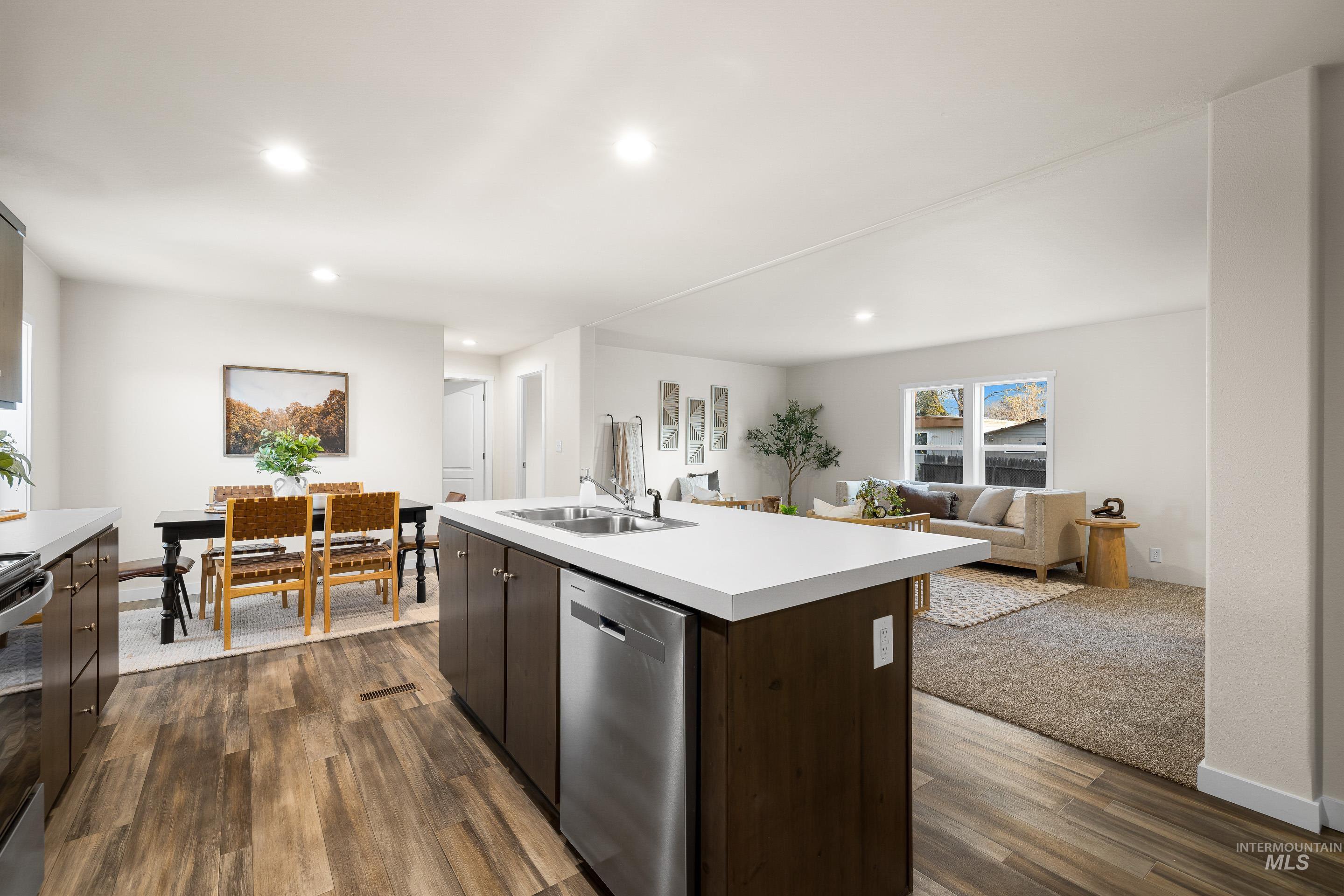 Kitchen featuring dark brown cabinetry, light countertops, open floor plan, stainless steel appliances, and a kitchen island with sink