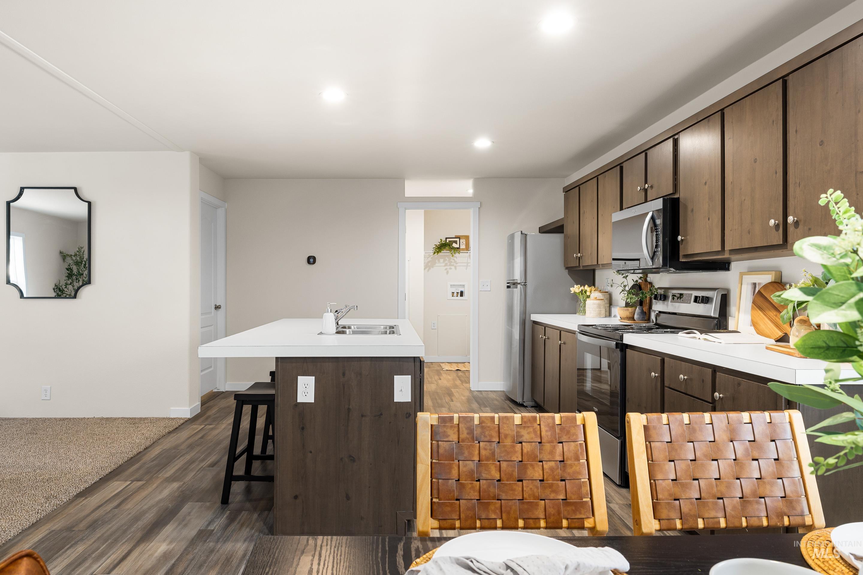 Kitchen featuring dark brown cabinetry, stainless steel appliances, light countertops, an island with sink, and recessed lighting
