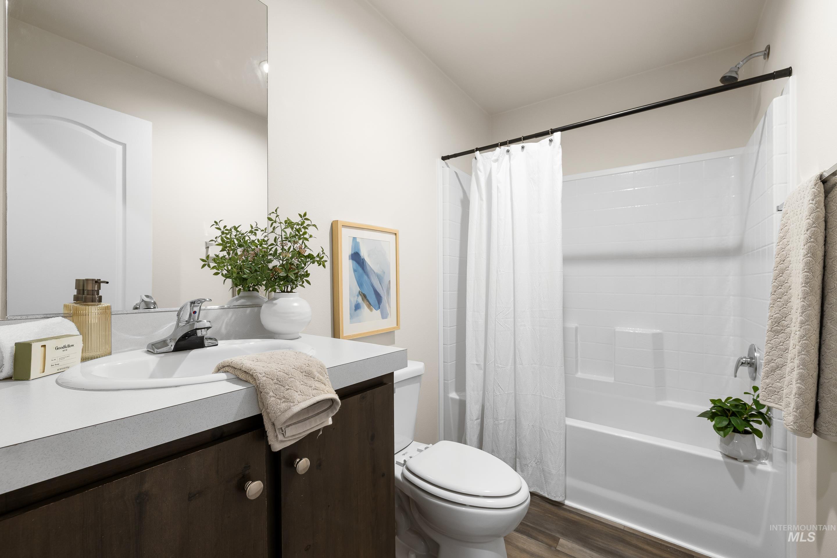 Bathroom featuring vanity, shower / bathtub combination with curtain, and dark wood-style flooring