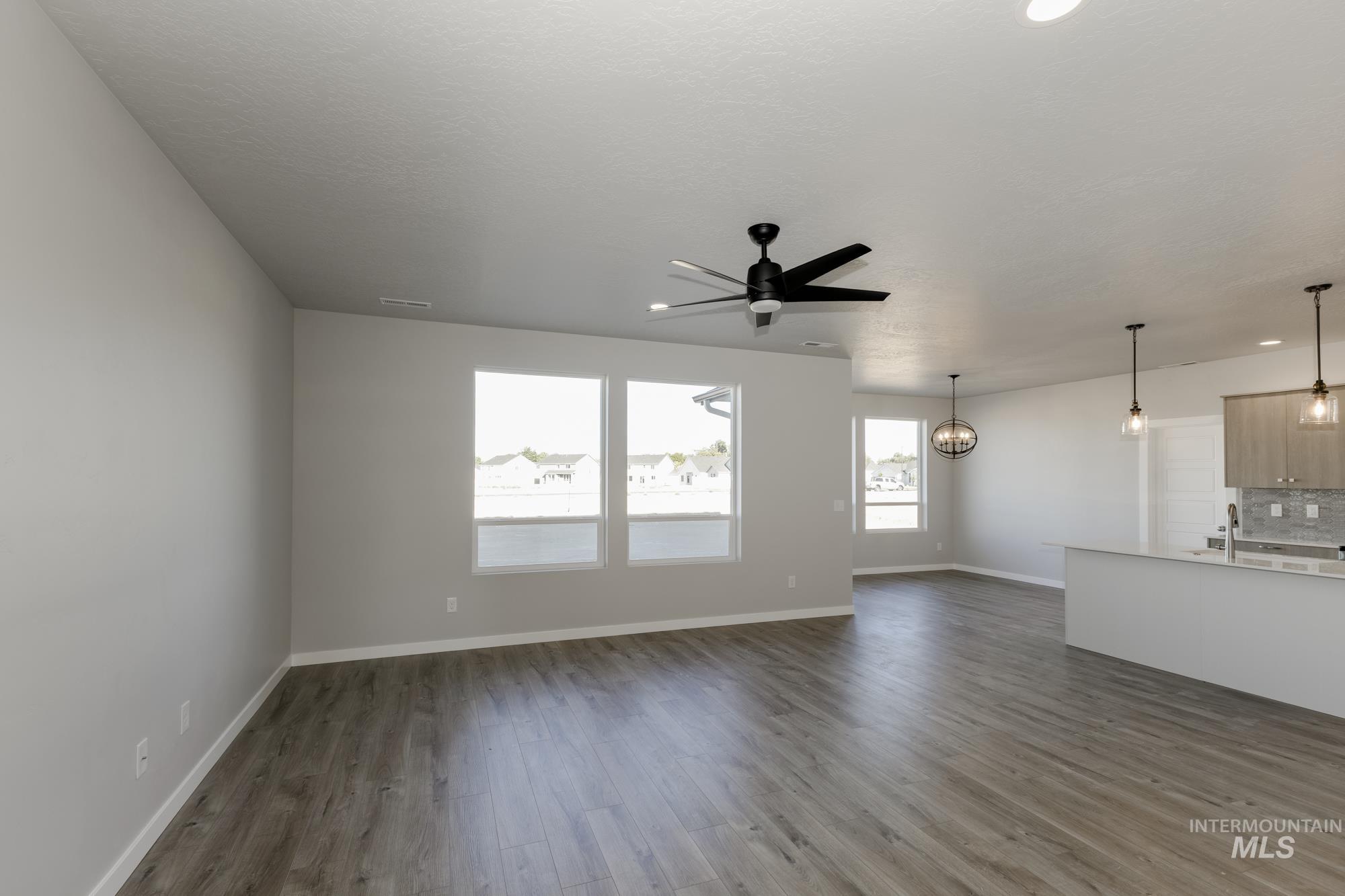 Unfurnished living room featuring dark wood finished floors, ceiling fan, and a chandelier