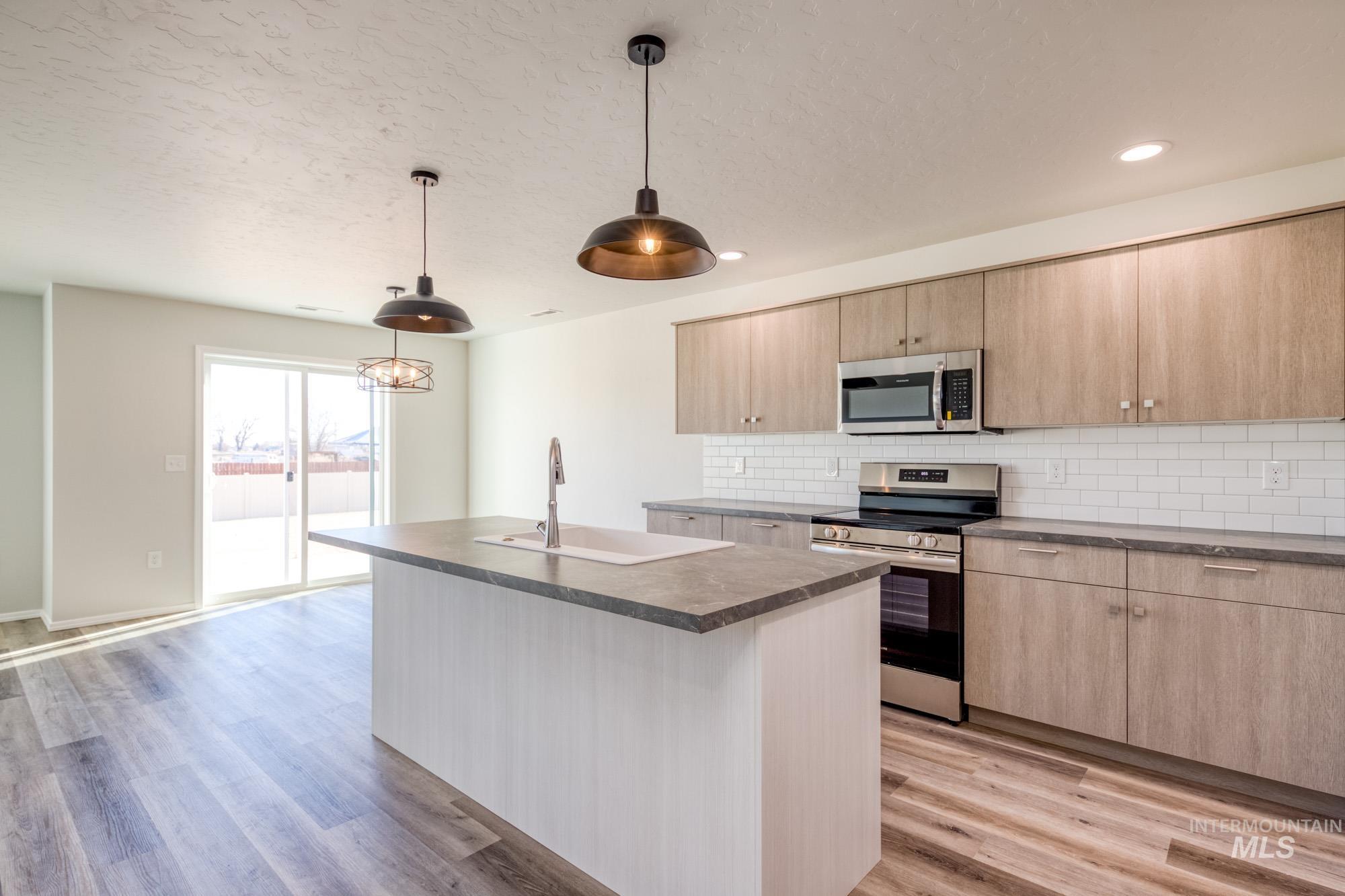 Kitchen with light brown cabinets, stainless steel appliances, a center island with sink, decorative backsplash, and a textured ceiling