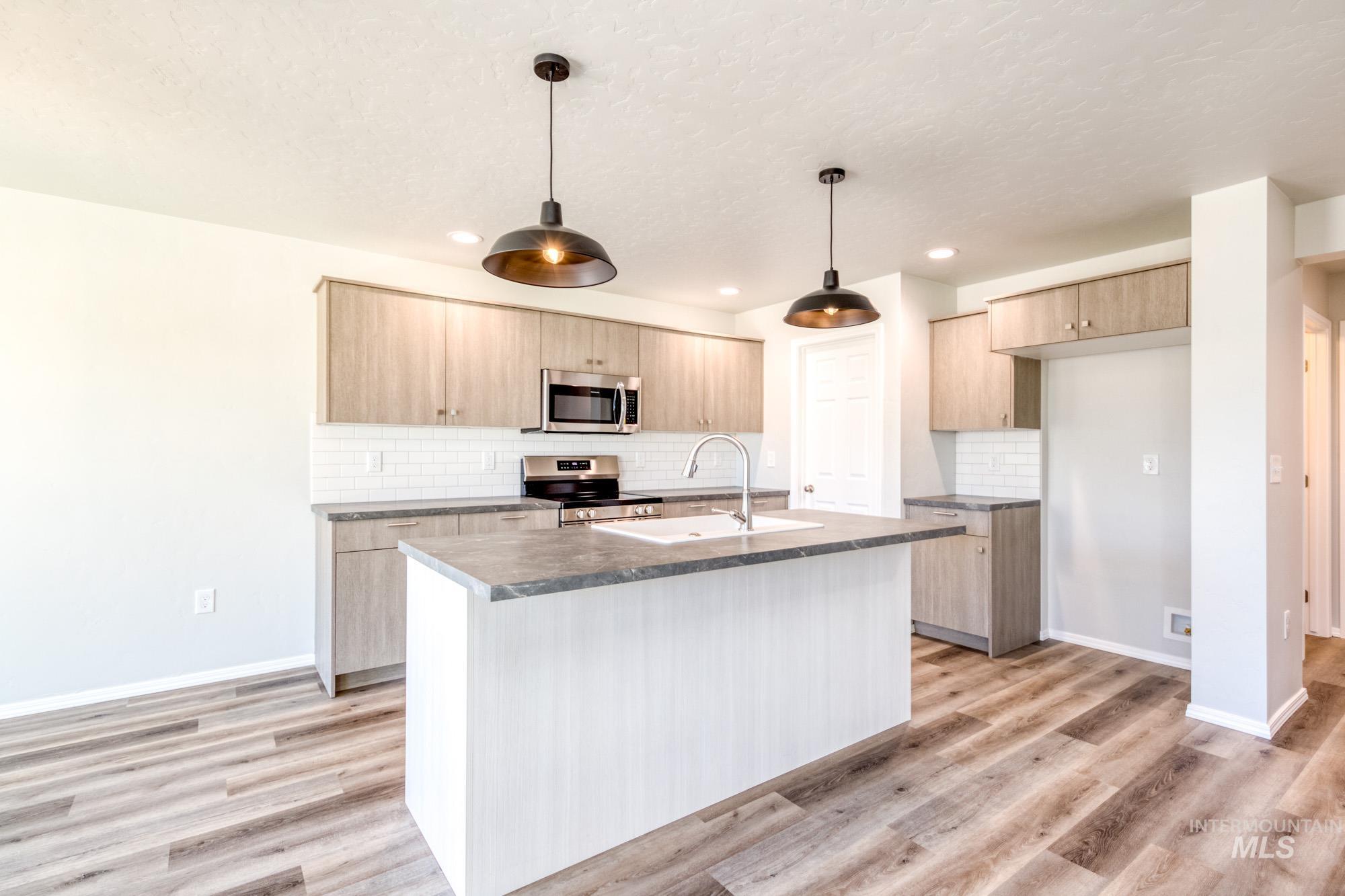 Kitchen with light brown cabinetry, decorative backsplash, appliances with stainless steel finishes, pendant lighting, and light wood finished floors