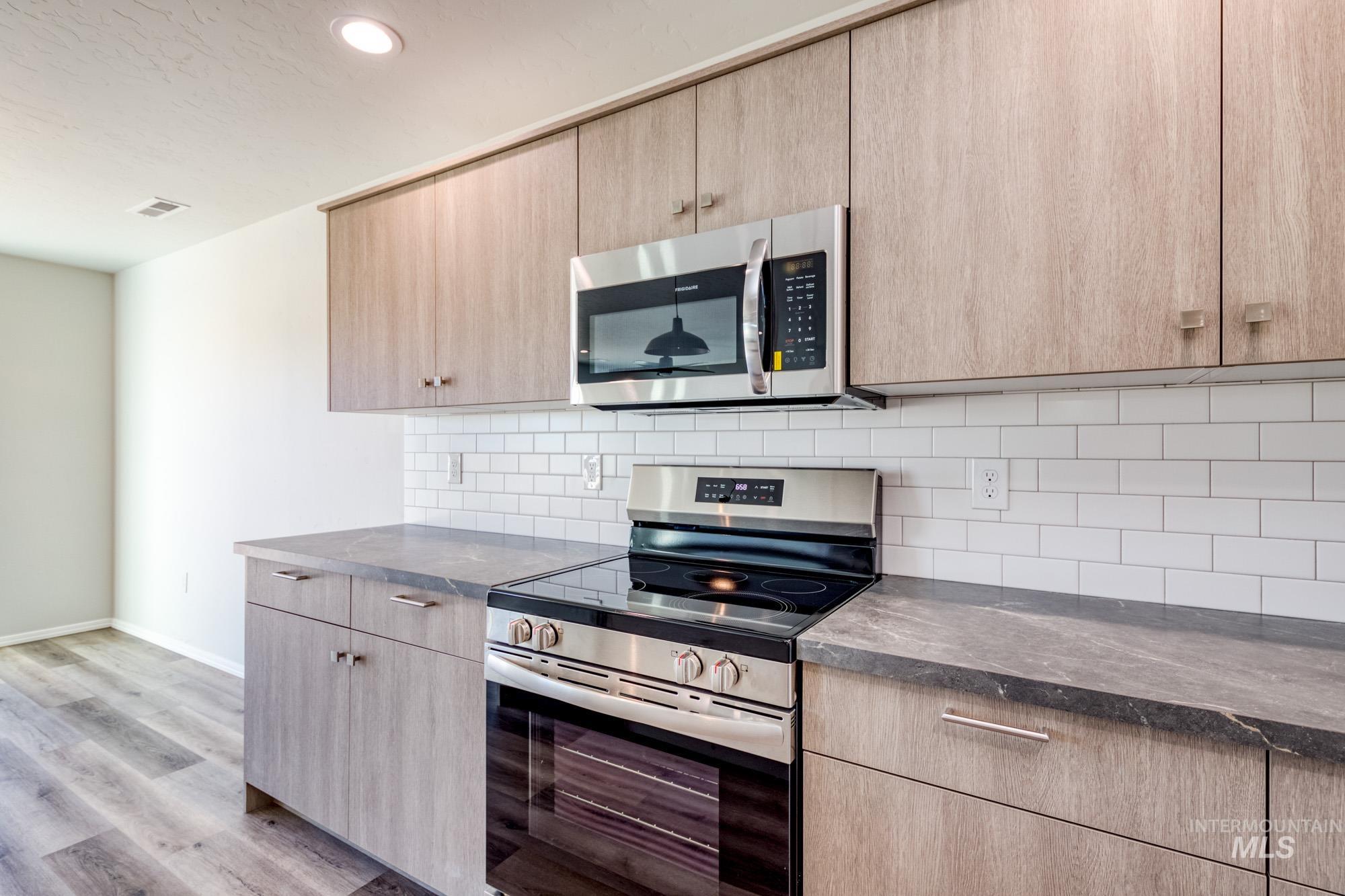 Kitchen featuring stainless steel appliances, light brown cabinetry, decorative backsplash, light wood-style floors, and recessed lighting