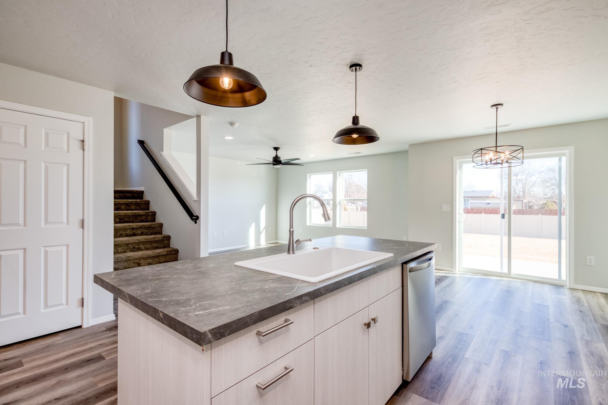 Kitchen featuring dark countertops, light wood-style flooring, decorative light fixtures, open floor plan, and stainless steel dishwasher