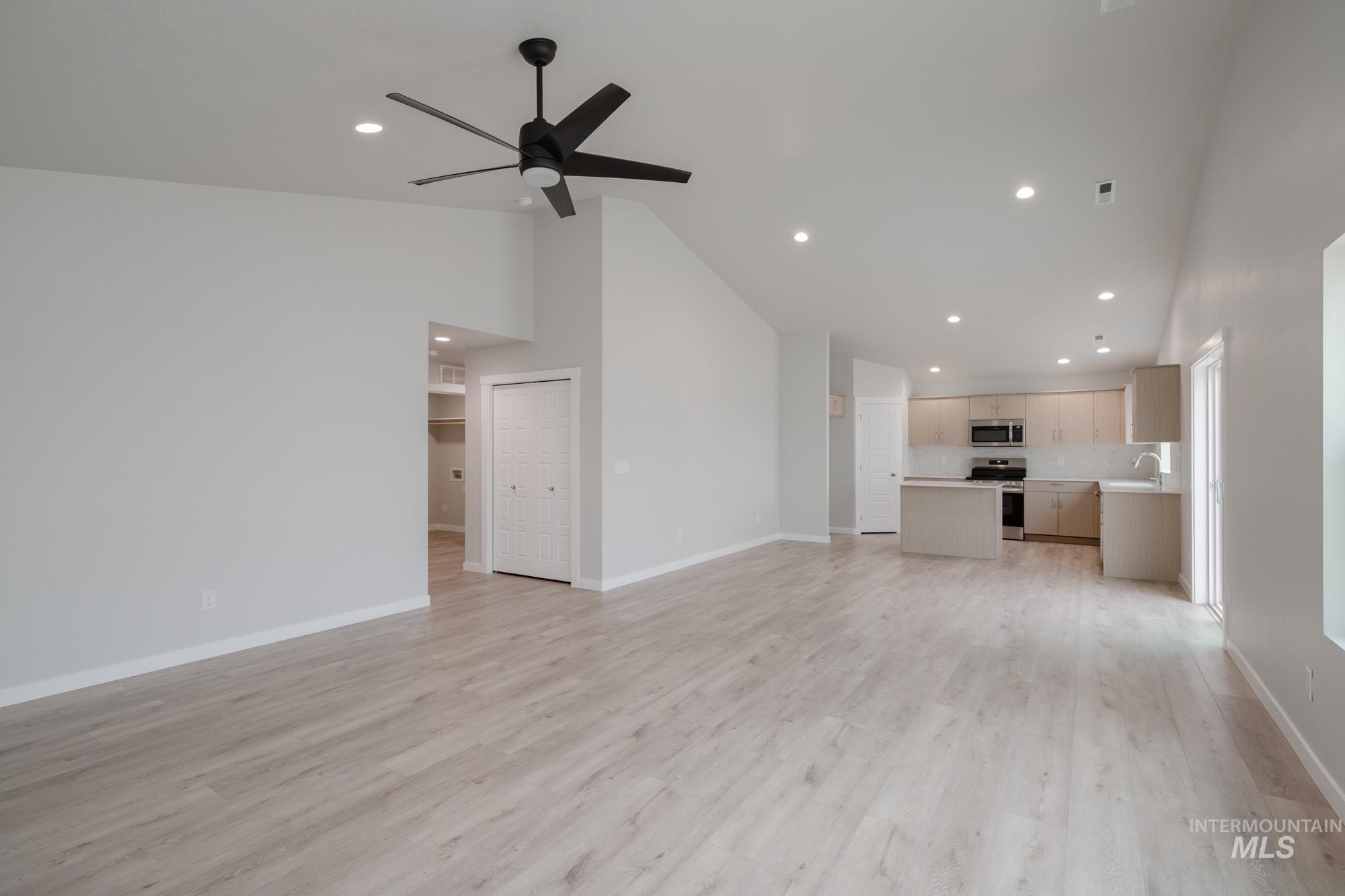 Unfurnished living room with light wood finished floors, recessed lighting, high vaulted ceiling, and a ceiling fan