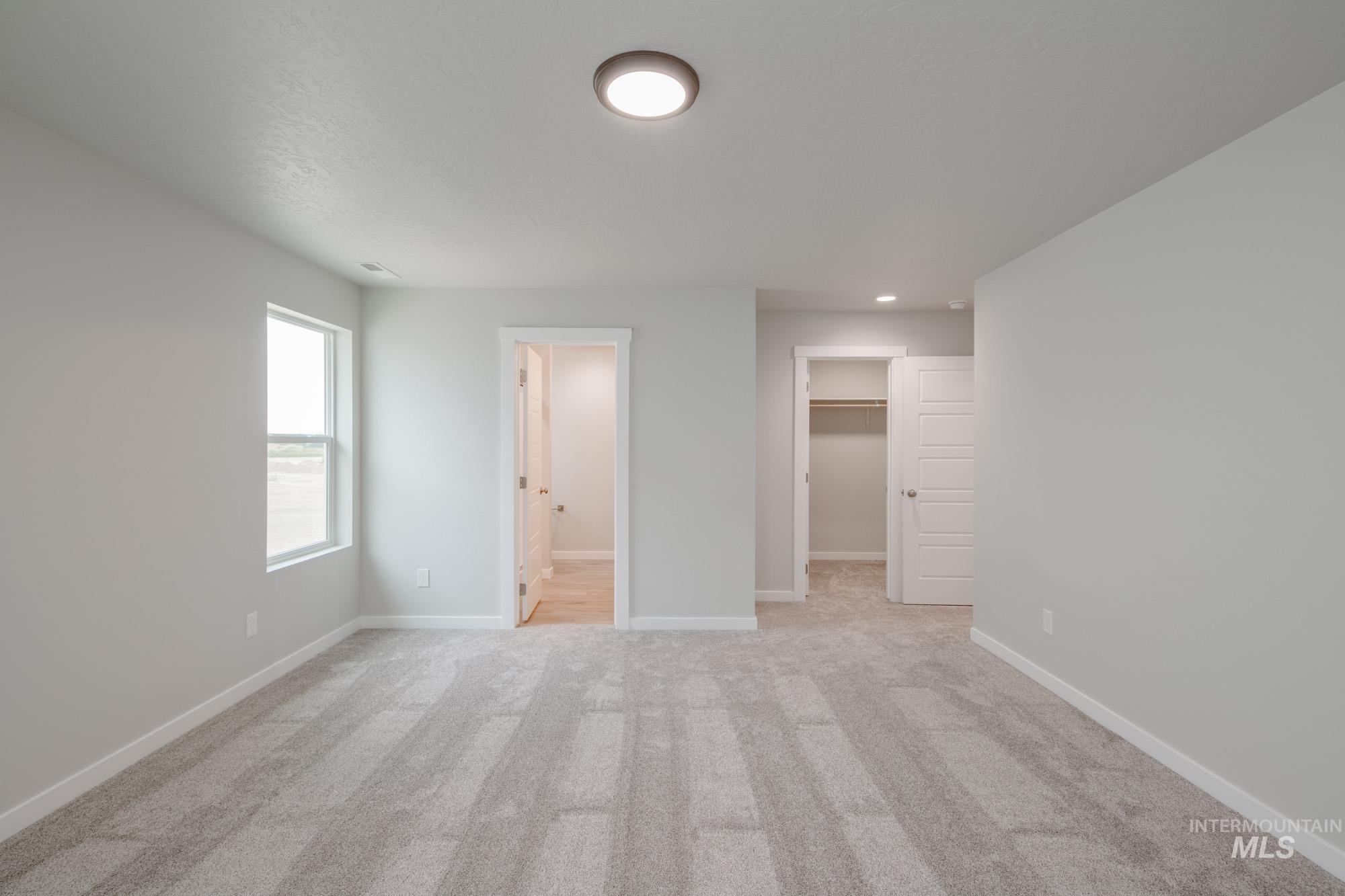 Unfurnished bedroom with light colored carpet, a spacious closet, and ensuite bath