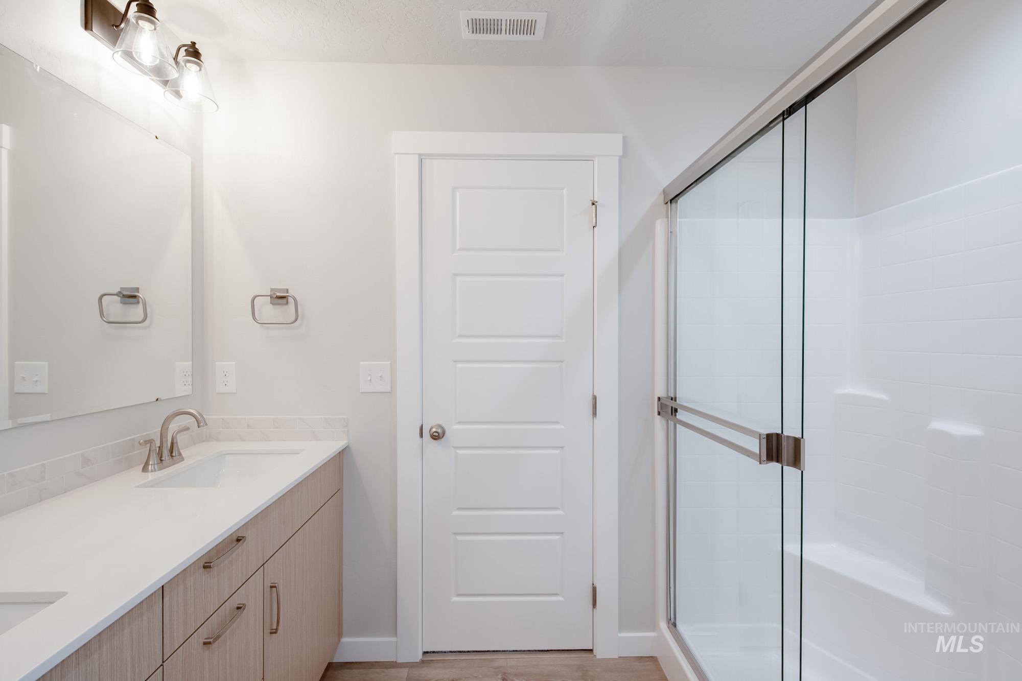 Bathroom featuring double vanity, a stall shower, and light wood-type flooring
