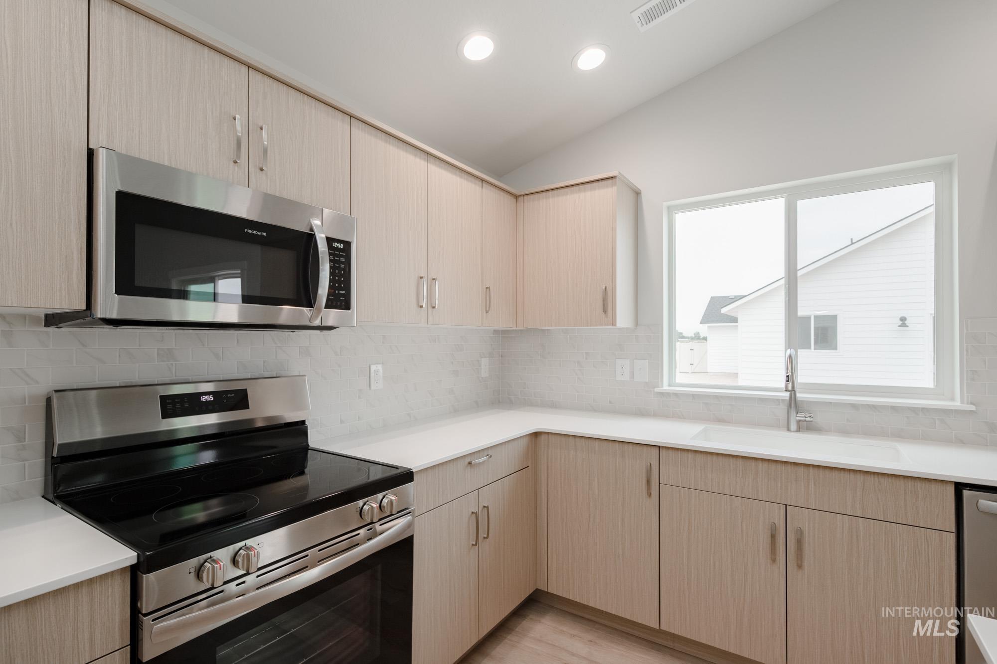 Kitchen with stainless steel appliances, light brown cabinetry, tasteful backsplash, recessed lighting, and lofted ceiling