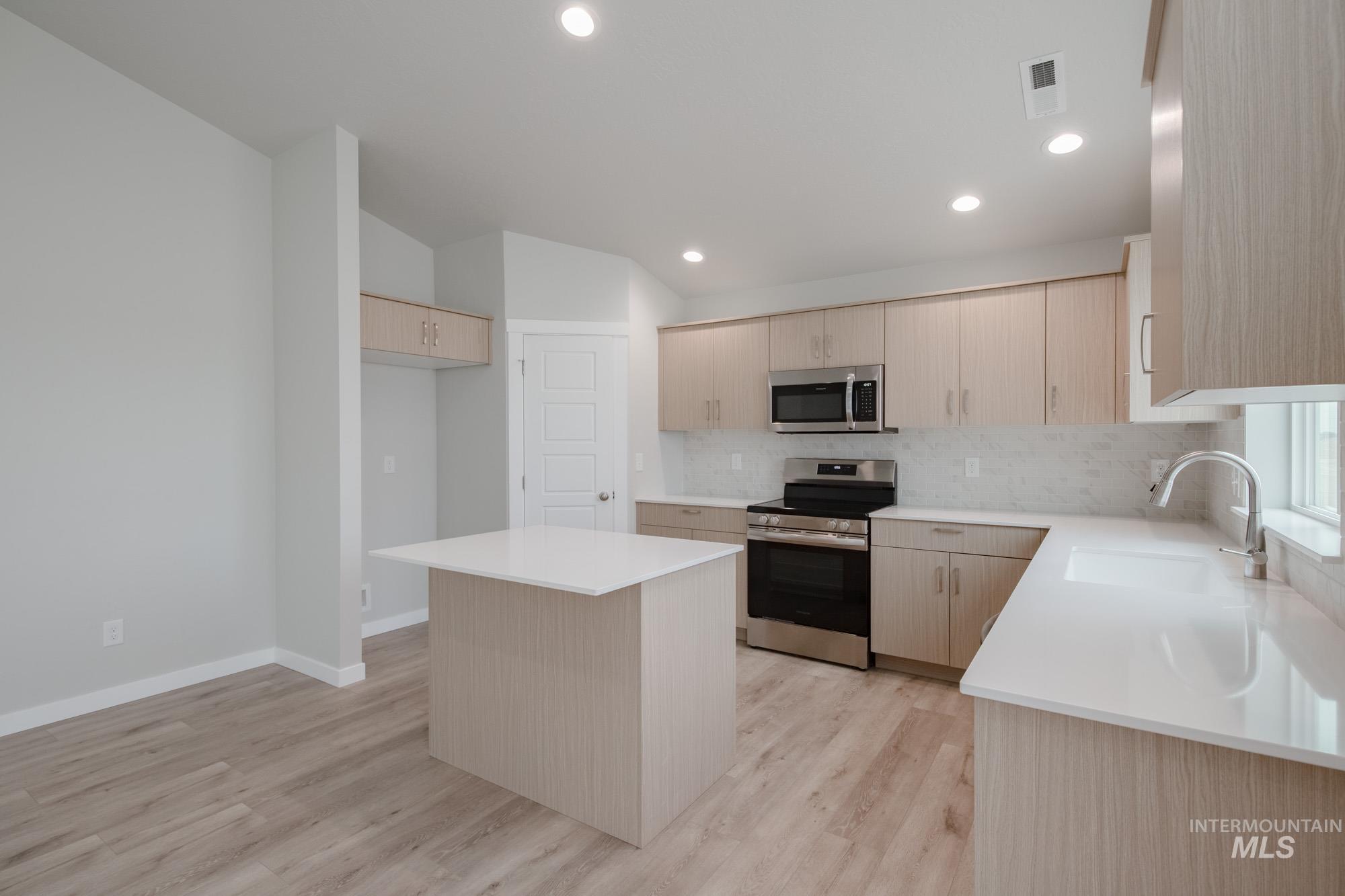 Kitchen with a kitchen island, stainless steel appliances, decorative backsplash, light brown cabinets, and light wood-style floors