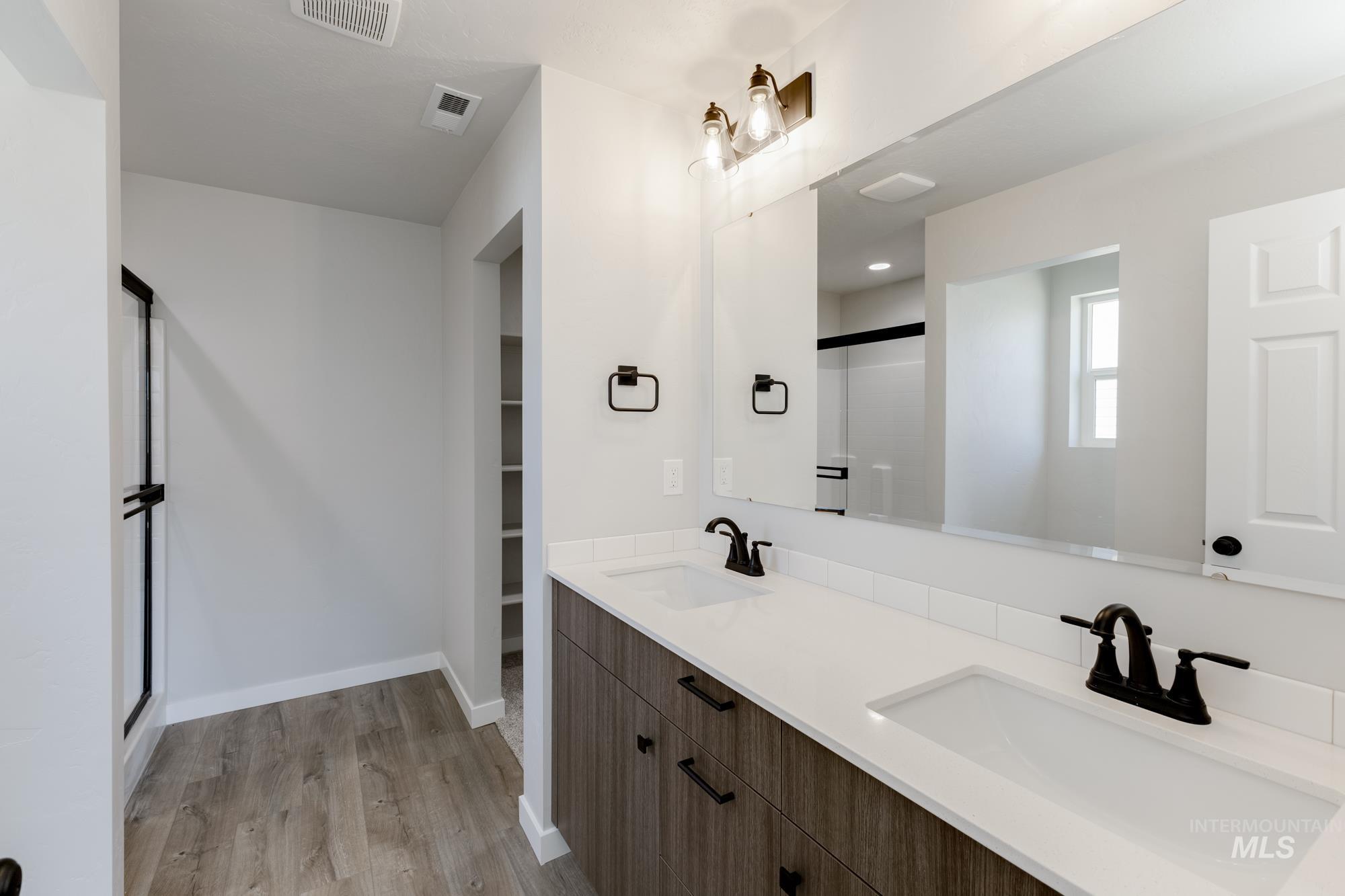Bathroom featuring a shower stall, double vanity, light wood-type flooring, and a spacious closet