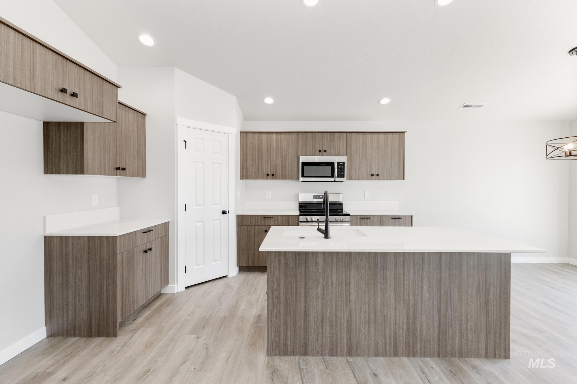 Kitchen with light wood-style floors, modern cabinets, appliances with stainless steel finishes, brown cabinets, and recessed lighting