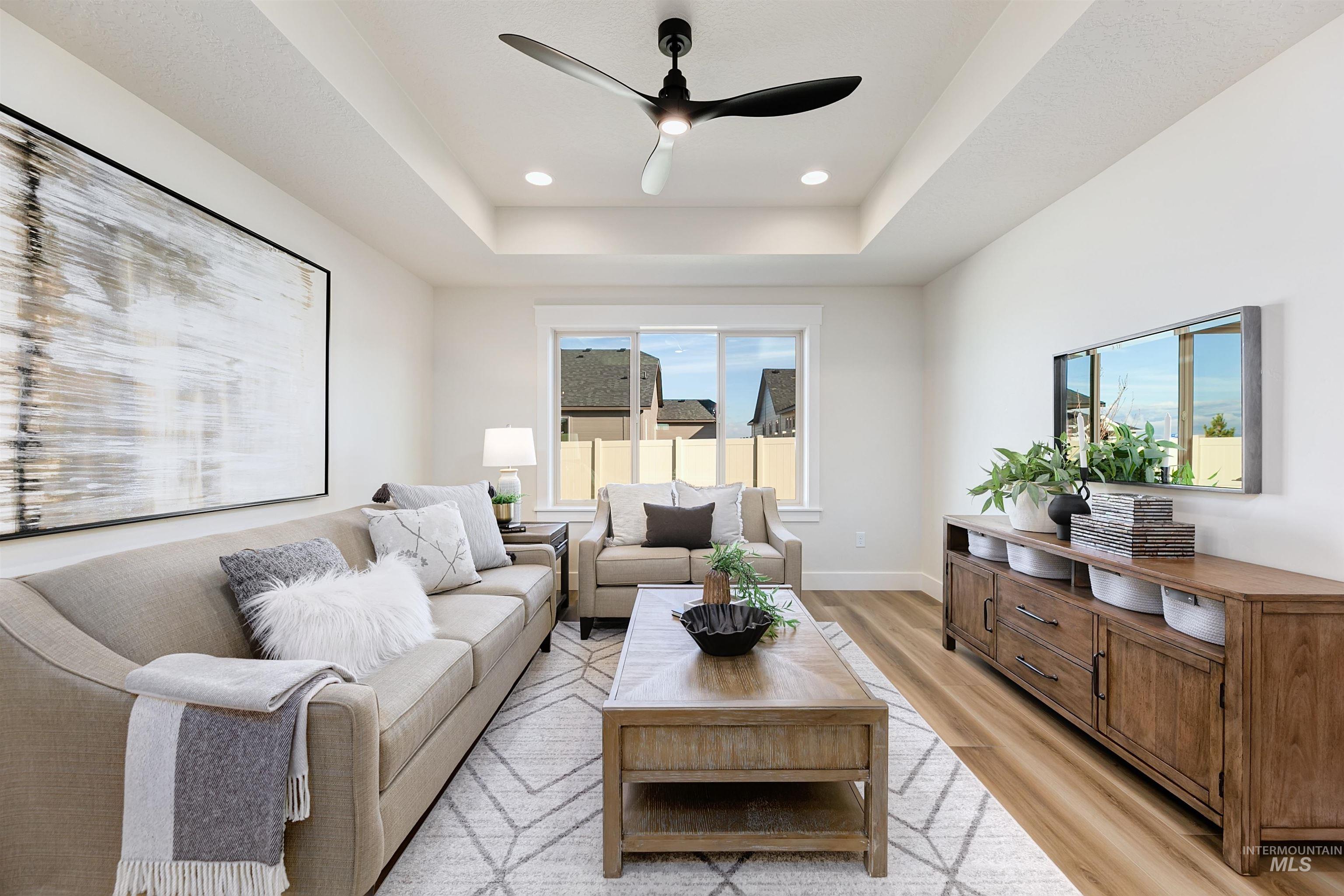 Living area with light wood finished floors, ceiling fan, recessed lighting, and a tray ceiling