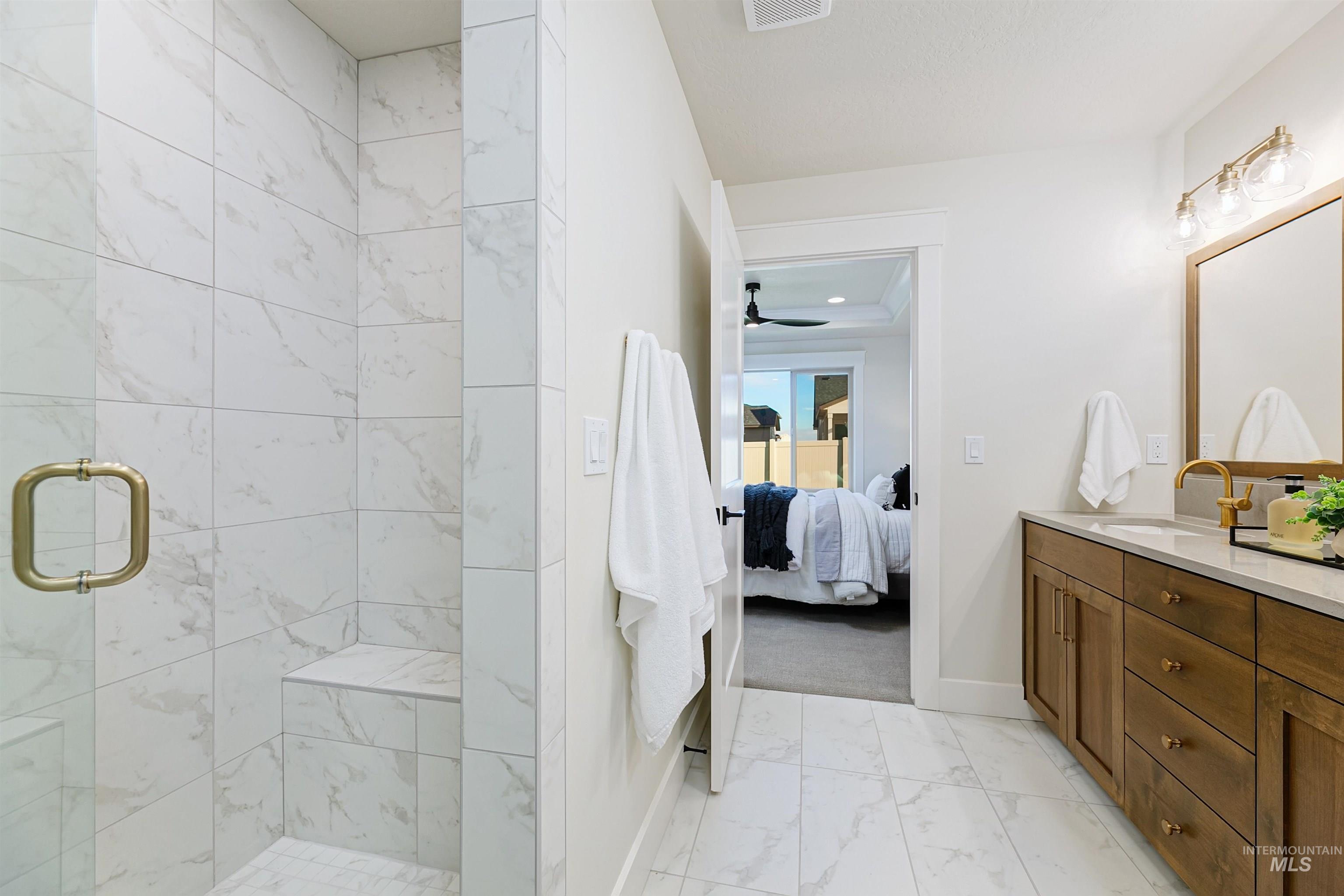 Full bath with light marble finish floors, vanity, a marble finish shower, ensuite bathroom, and ceiling fan