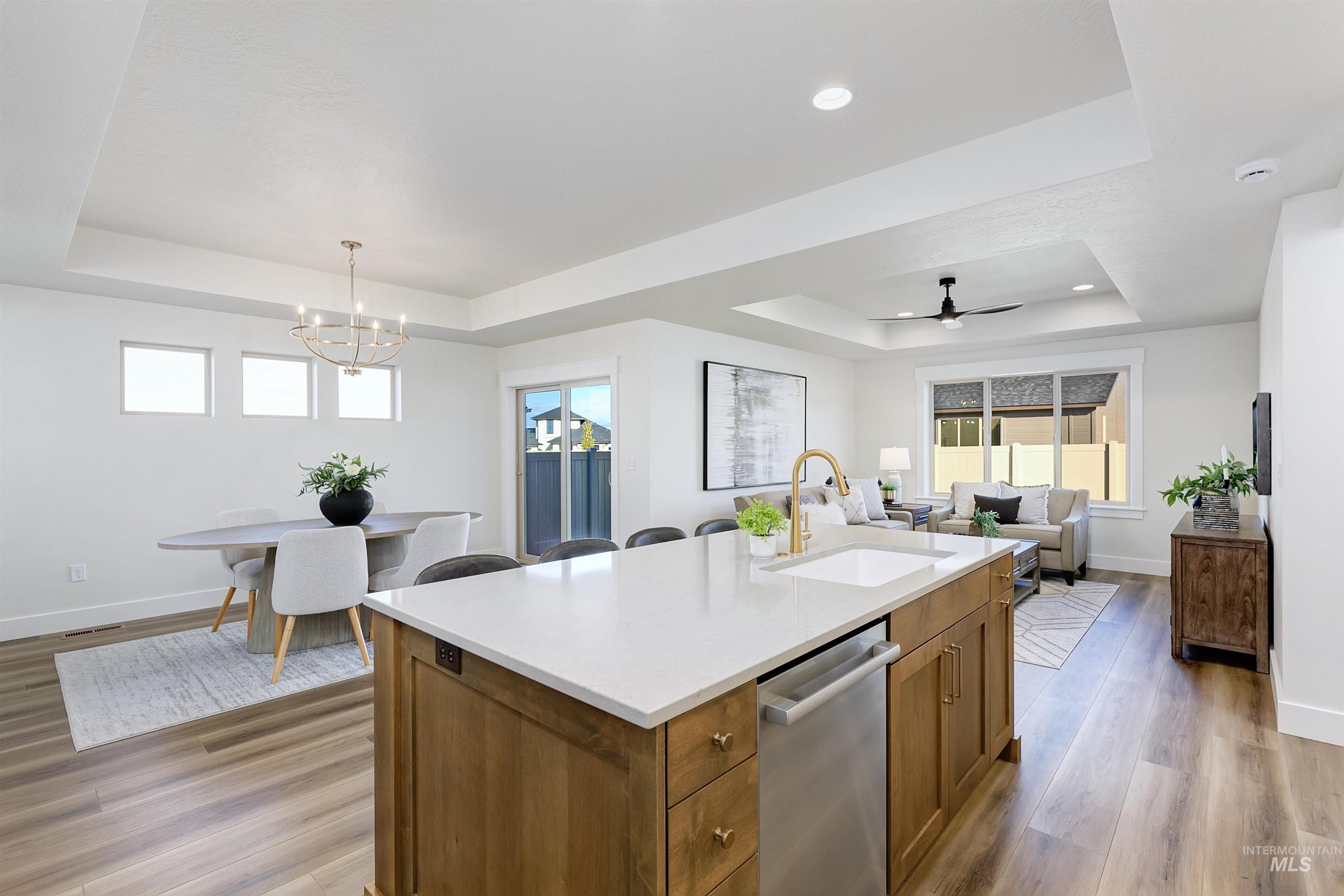 Kitchen featuring brown cabinets, a raised ceiling, light wood-type flooring, light stone counters, and a kitchen island with sink