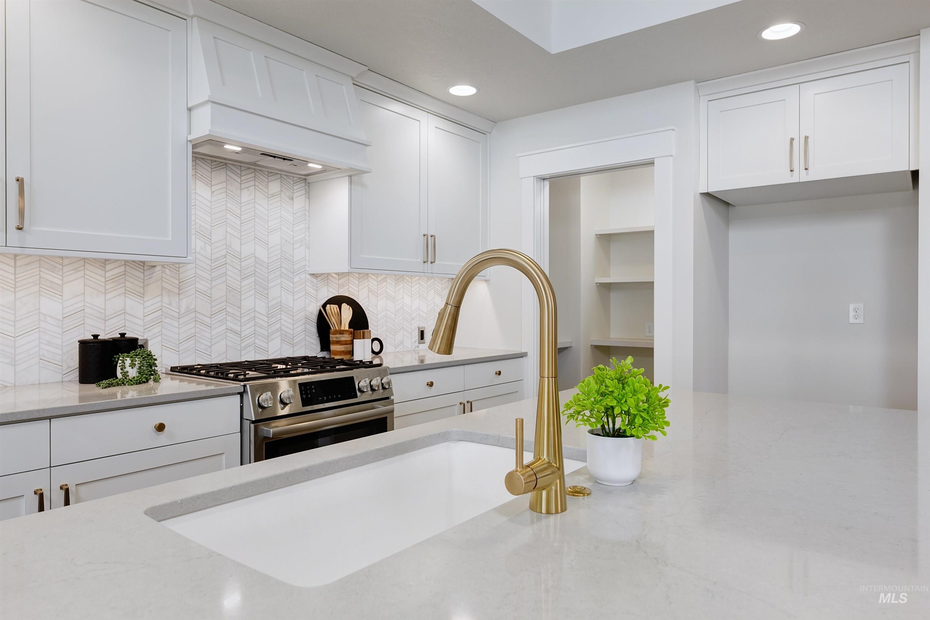 Kitchen featuring custom range hood, white cabinetry, stainless steel range with gas stovetop, tasteful backsplash, and recessed lighting