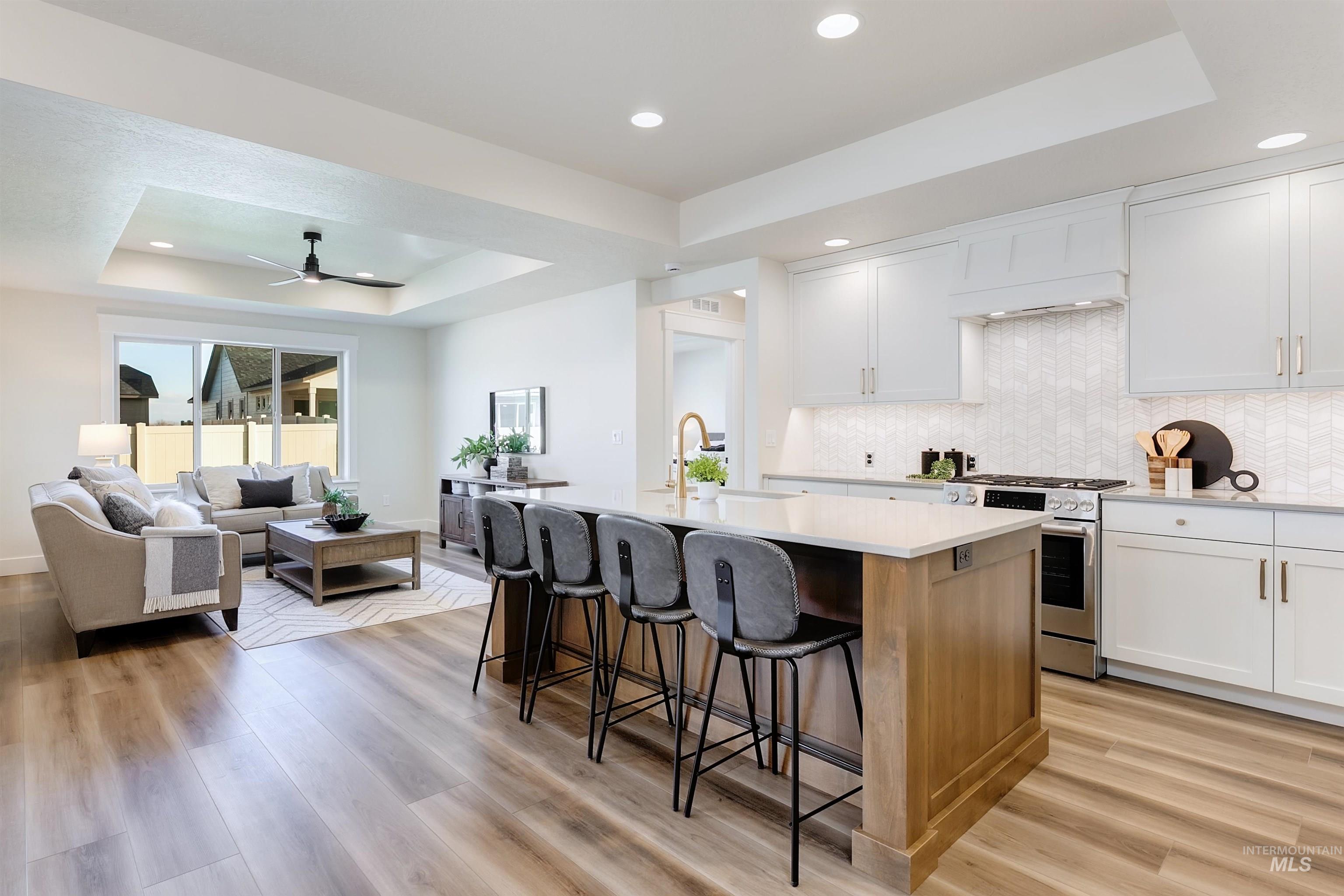 Kitchen featuring a tray ceiling, white cabinetry, stainless steel gas stove, and recessed lighting