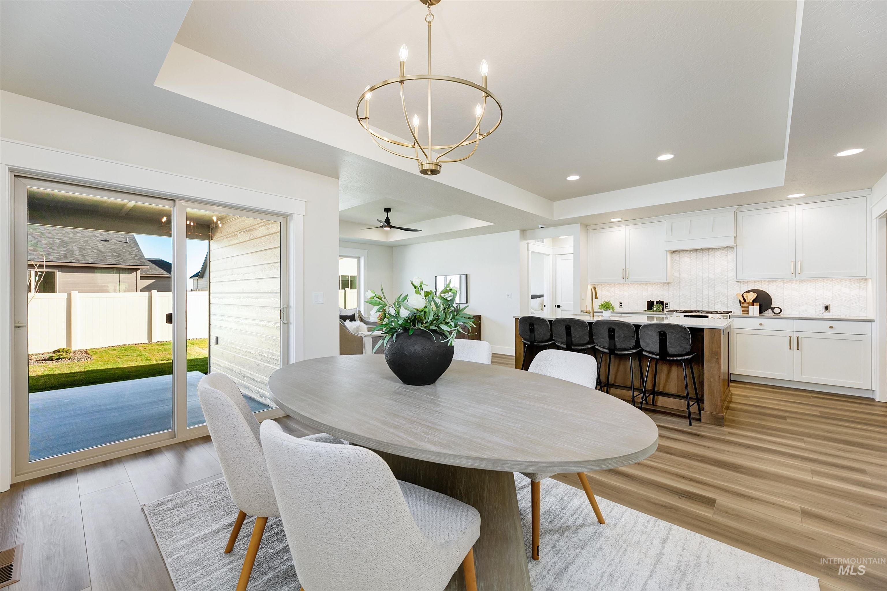 Dining space featuring a raised ceiling, light wood finished floors, a chandelier, a ceiling fan, and recessed lighting