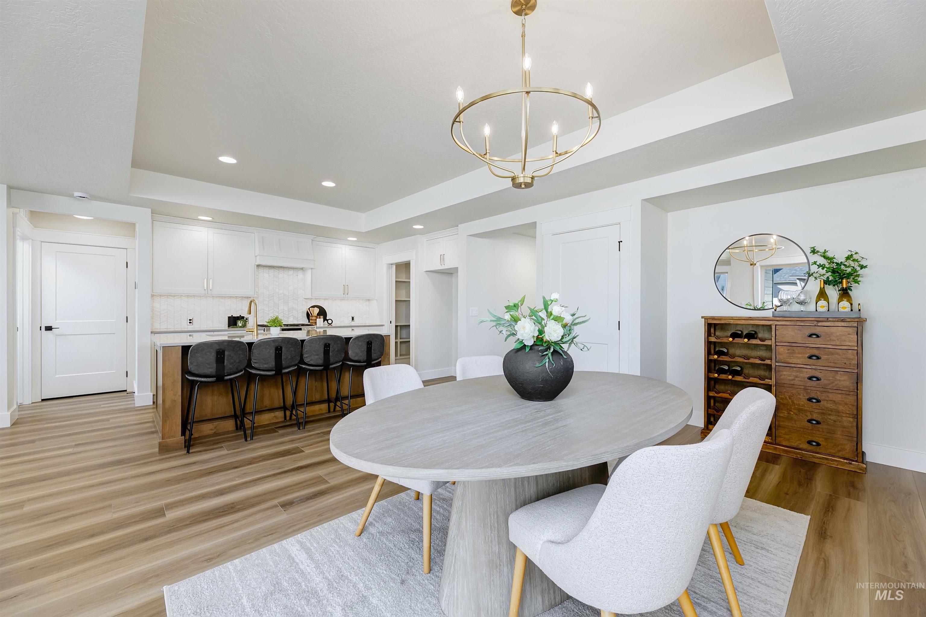 Dining room with a raised ceiling, light wood-type flooring, a chandelier, and recessed lighting