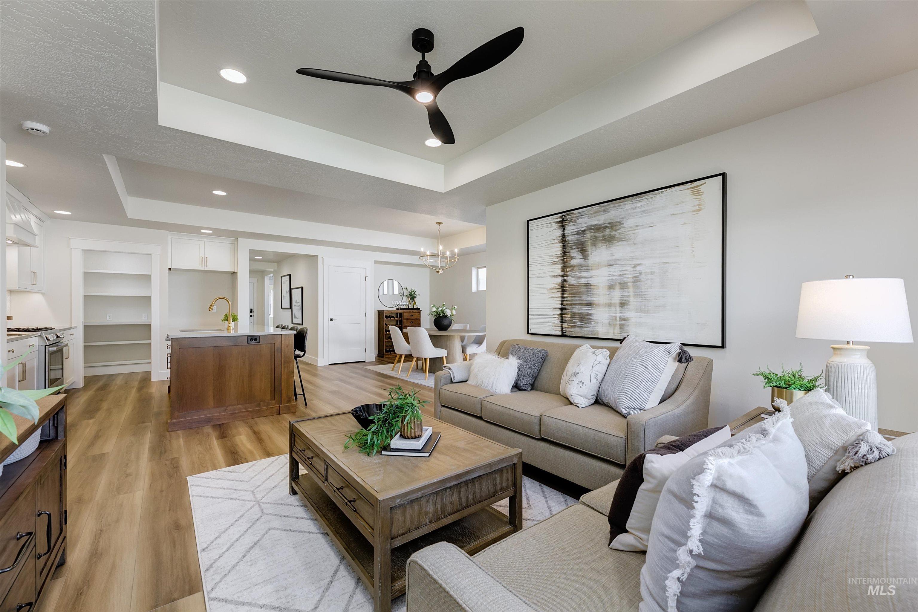 Living area with a ceiling fan, a tray ceiling, light wood-style floors, a chandelier, and recessed lighting