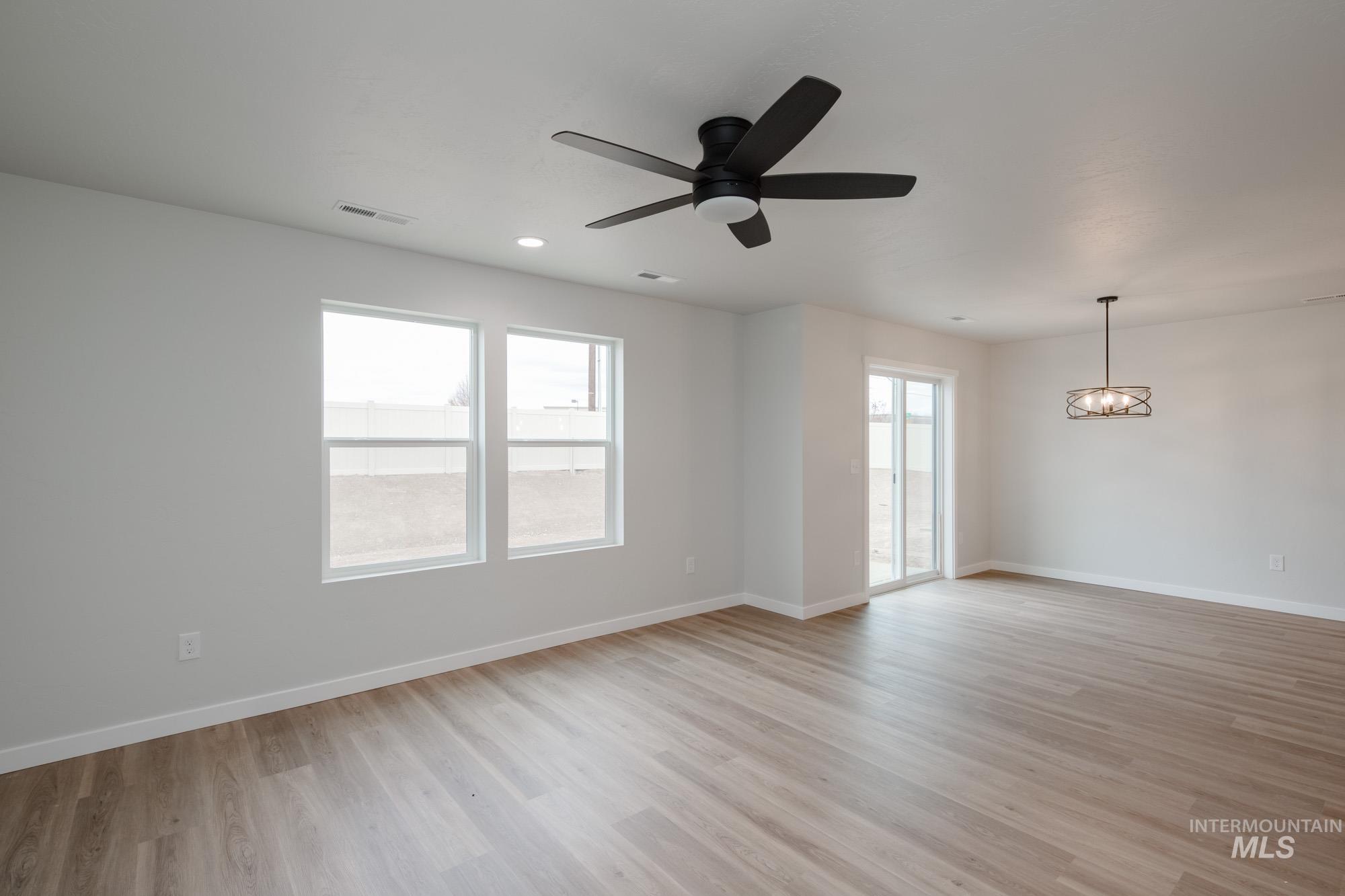 Empty room with plenty of natural light, light wood-style floors, a ceiling fan, and a chandelier