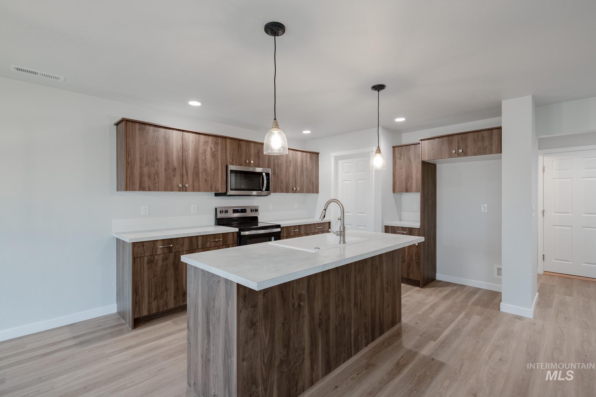 Kitchen featuring stainless steel appliances, light countertops, decorative light fixtures, light wood-style floors, and recessed lighting