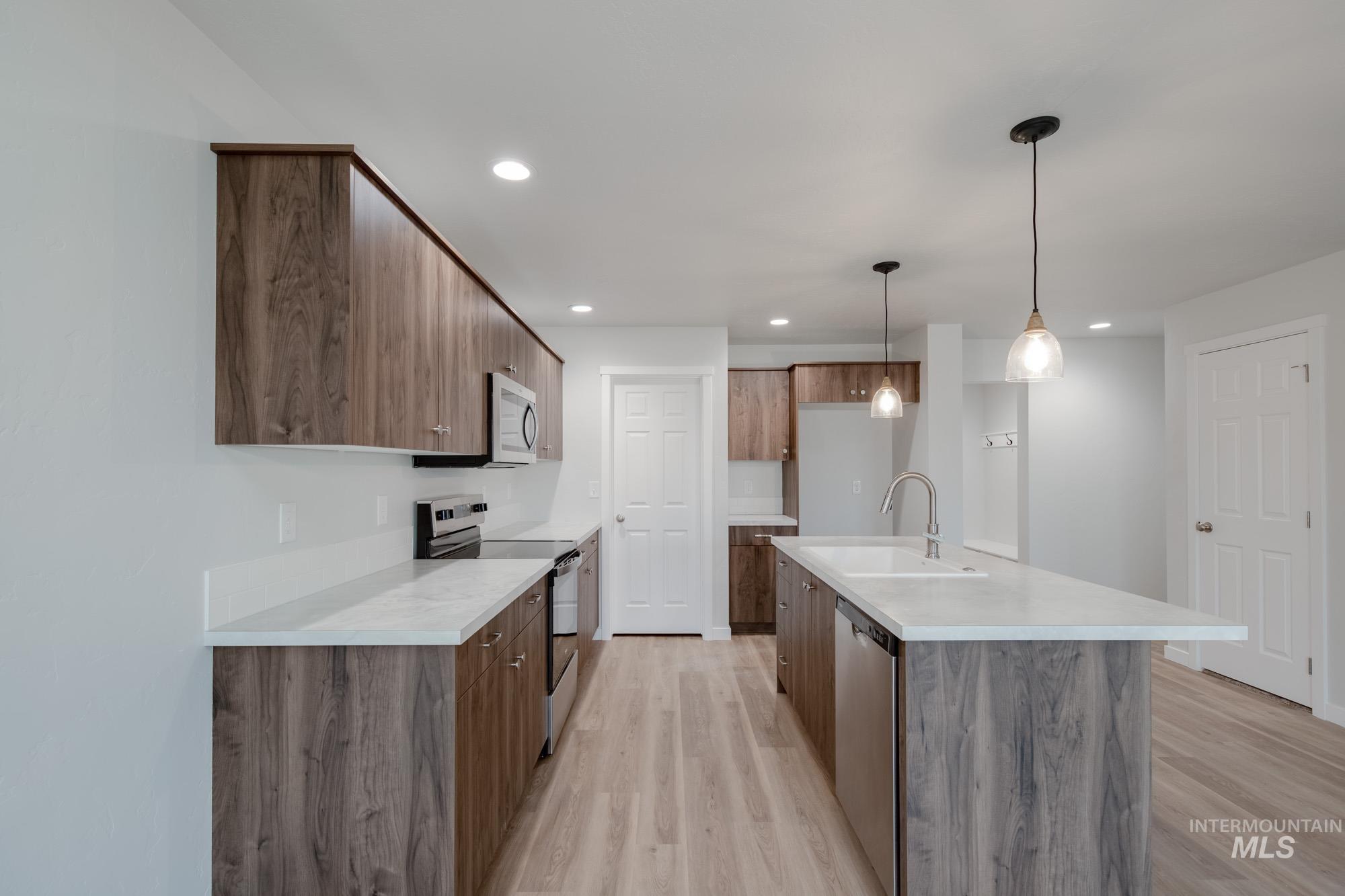 Kitchen featuring appliances with stainless steel finishes, light countertops, light wood-style floors, an island with sink, and hanging light fixtures