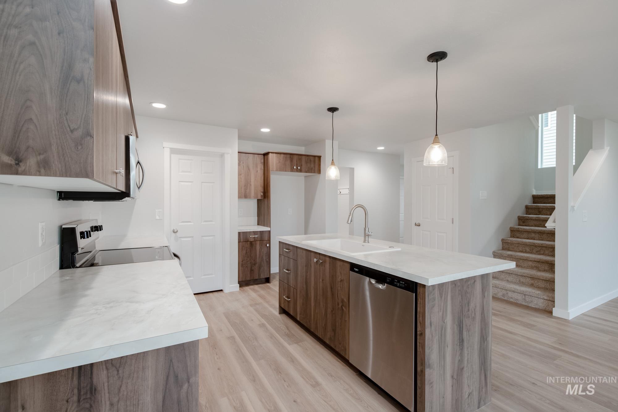 Kitchen with decorative light fixtures, light countertops, light wood-type flooring, stainless steel dishwasher, and an island with sink