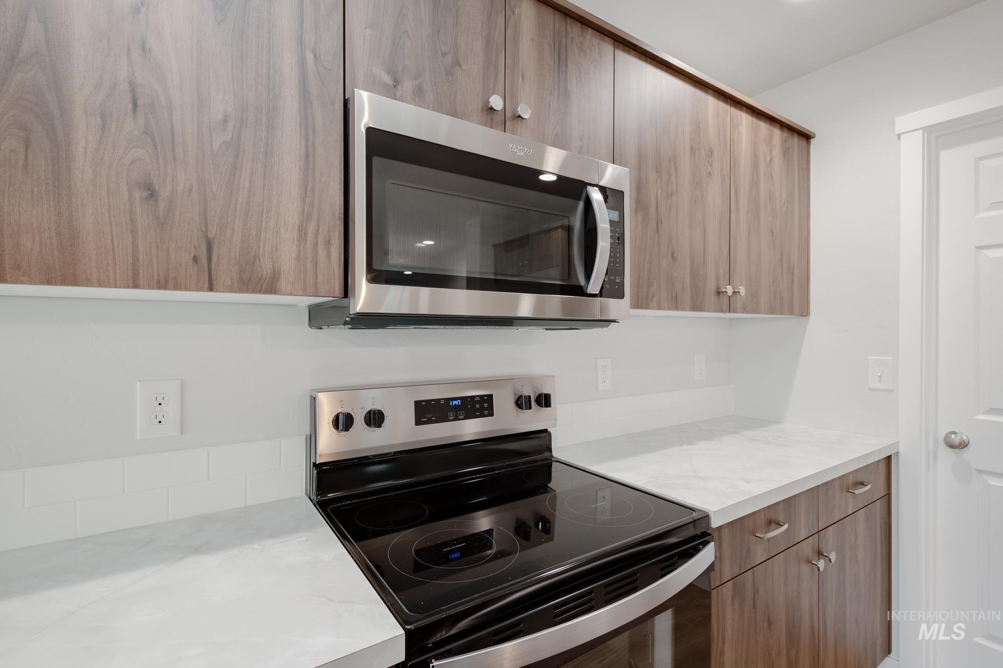 Kitchen with stainless steel appliances, light countertops, modern cabinets, and brown cabinetry