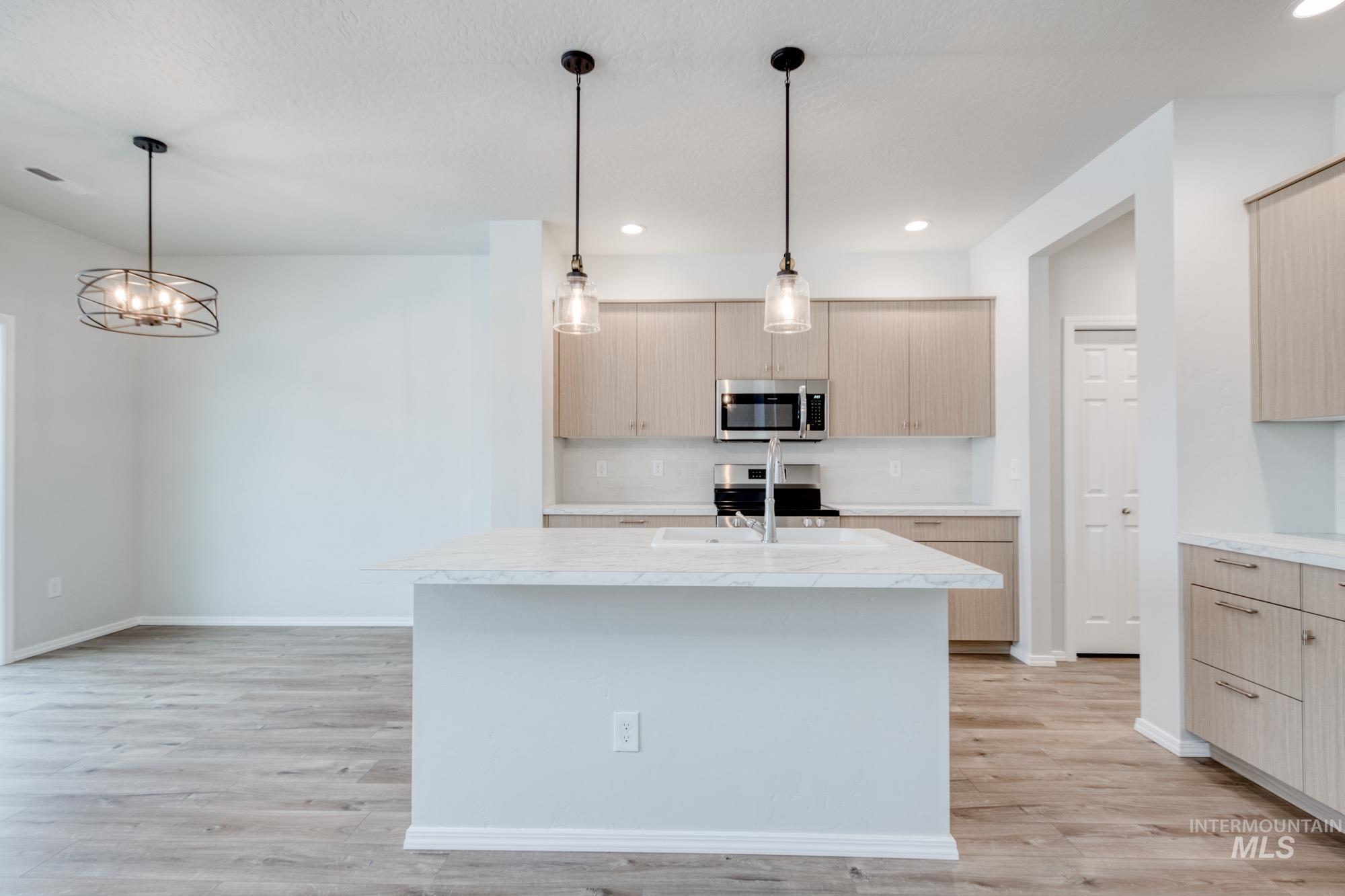Kitchen featuring stainless steel appliances, pendant lighting, an island with sink, light wood-style floors, and modern cabinets