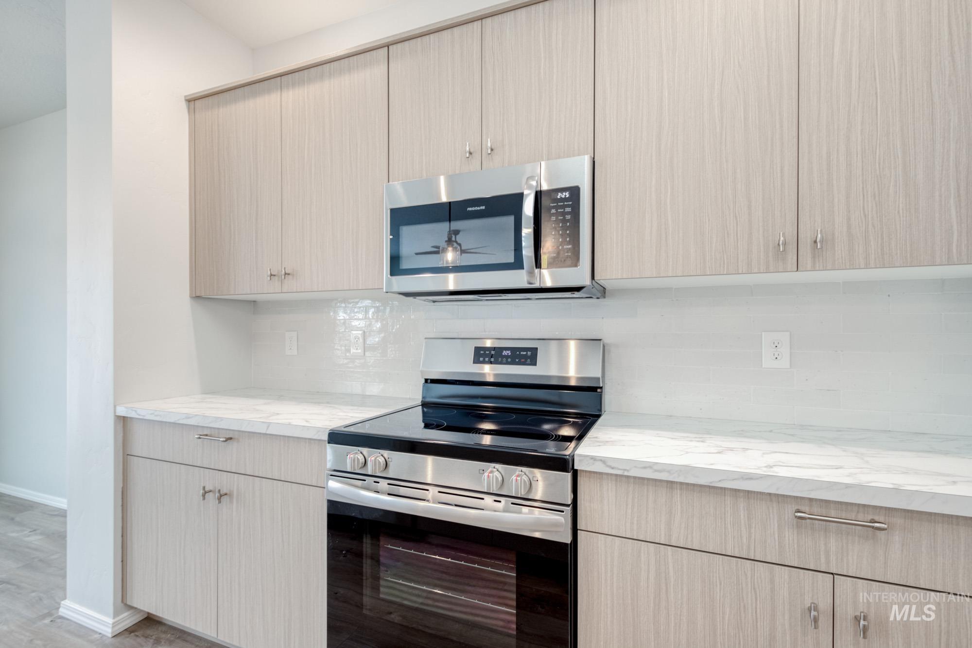 Kitchen with appliances with stainless steel finishes, tasteful backsplash, light stone countertops, and light brown cabinets