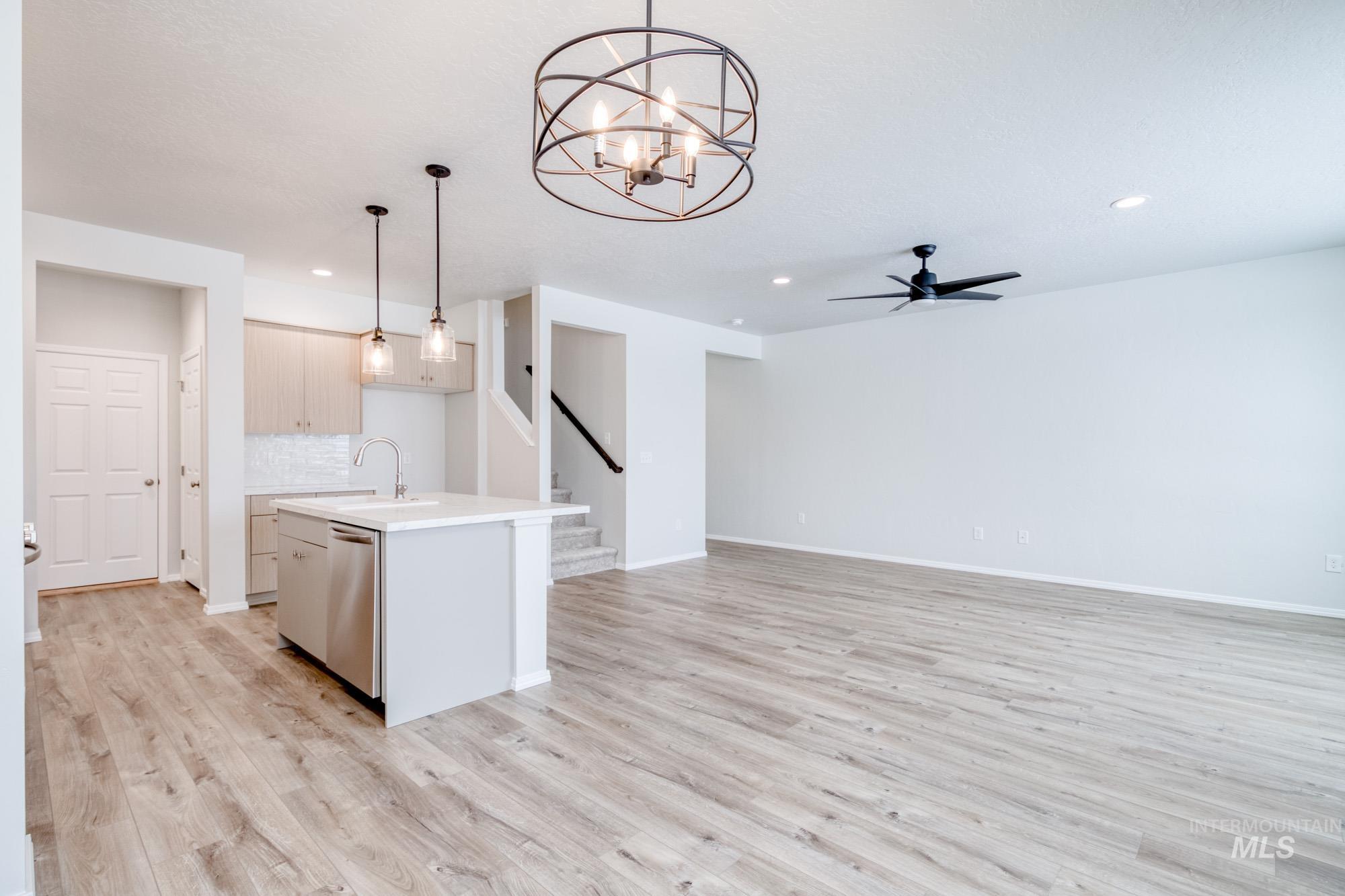 Kitchen with hanging light fixtures, a kitchen island with sink, ceiling fan, light wood finished floors, and a chandelier
