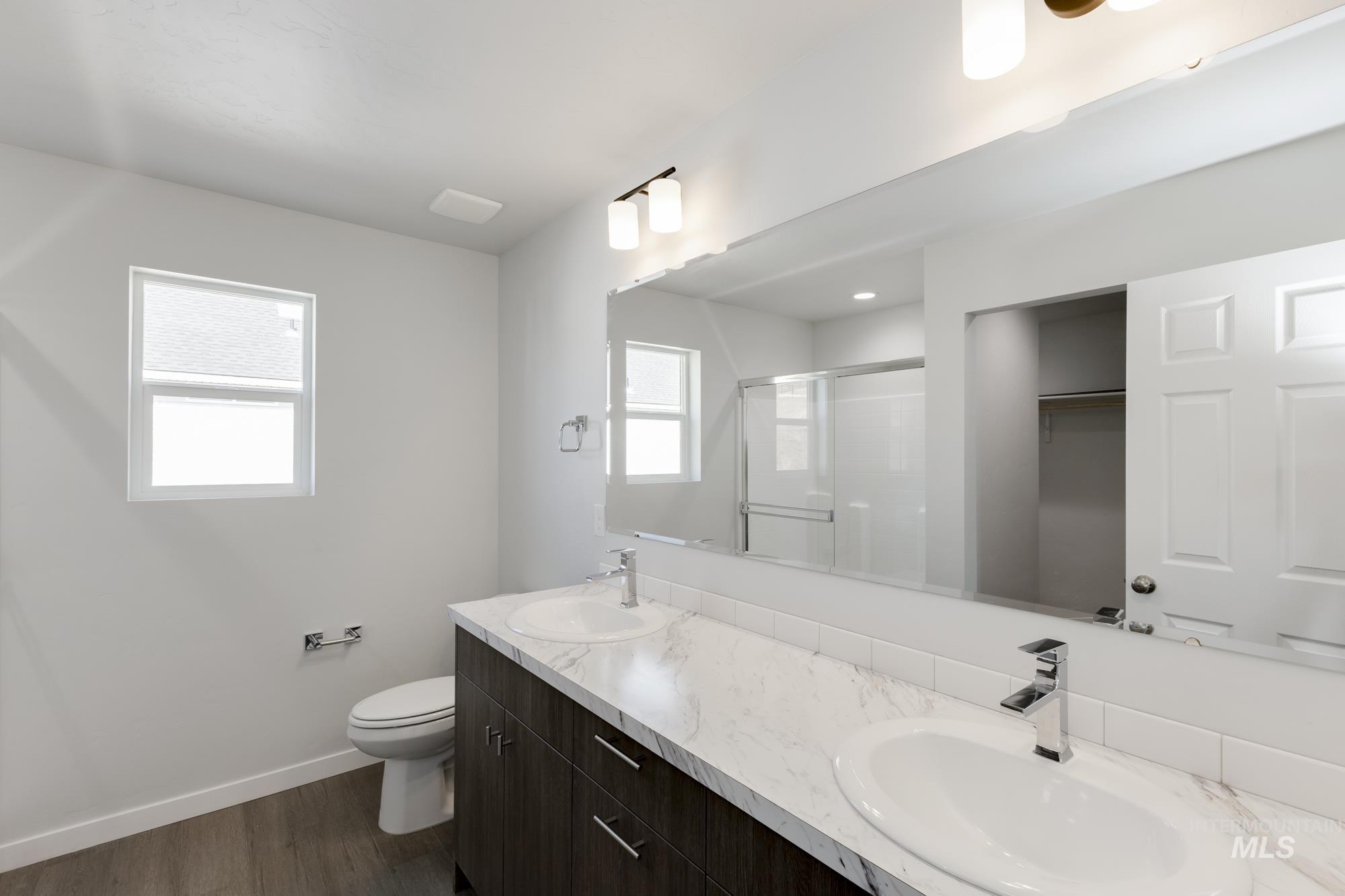 Full bath featuring a stall shower, dark wood-type flooring, double vanity, and a spacious closet