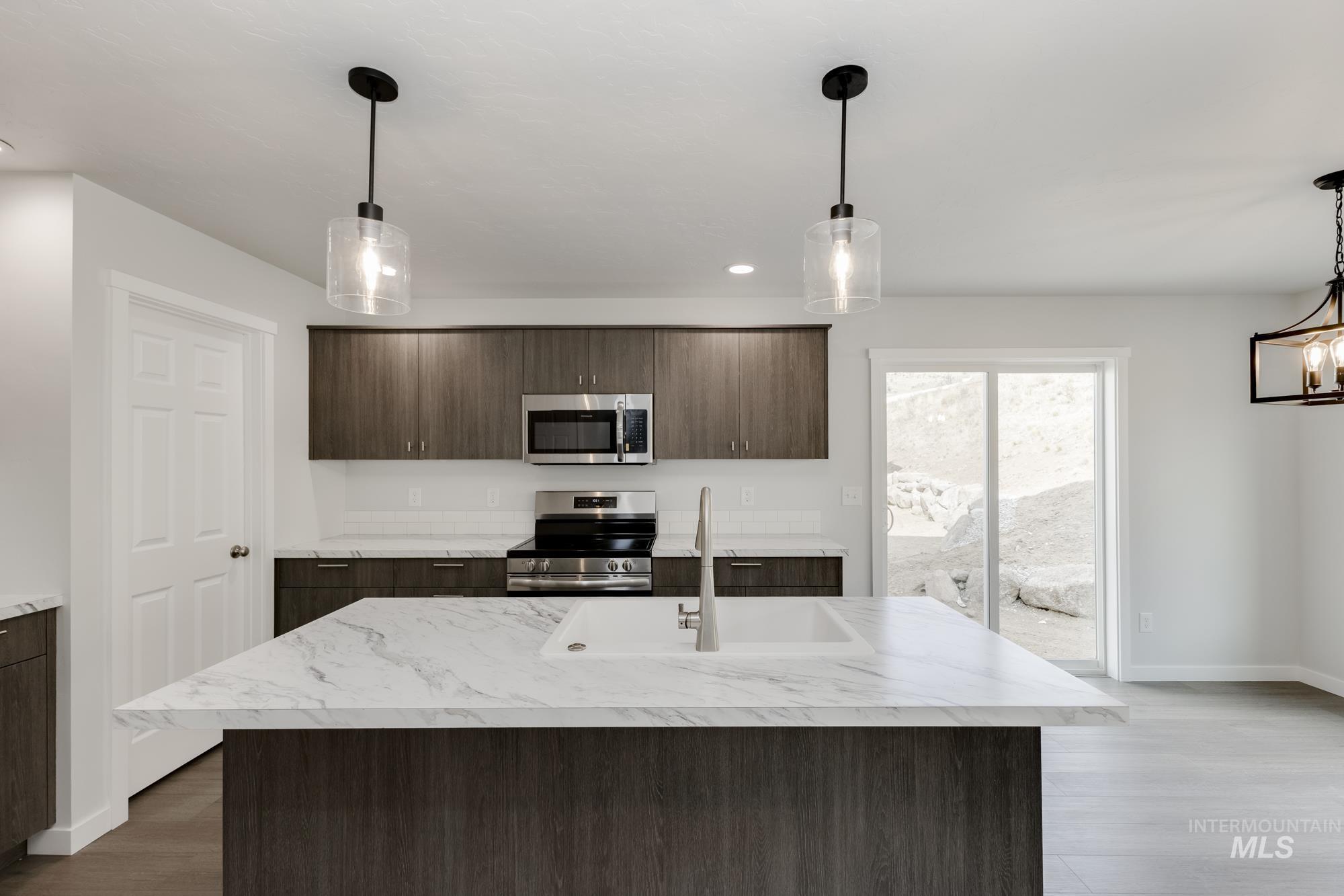 Kitchen with decorative light fixtures, dark brown cabinets, appliances with stainless steel finishes, a center island with sink, and dark wood finished floors