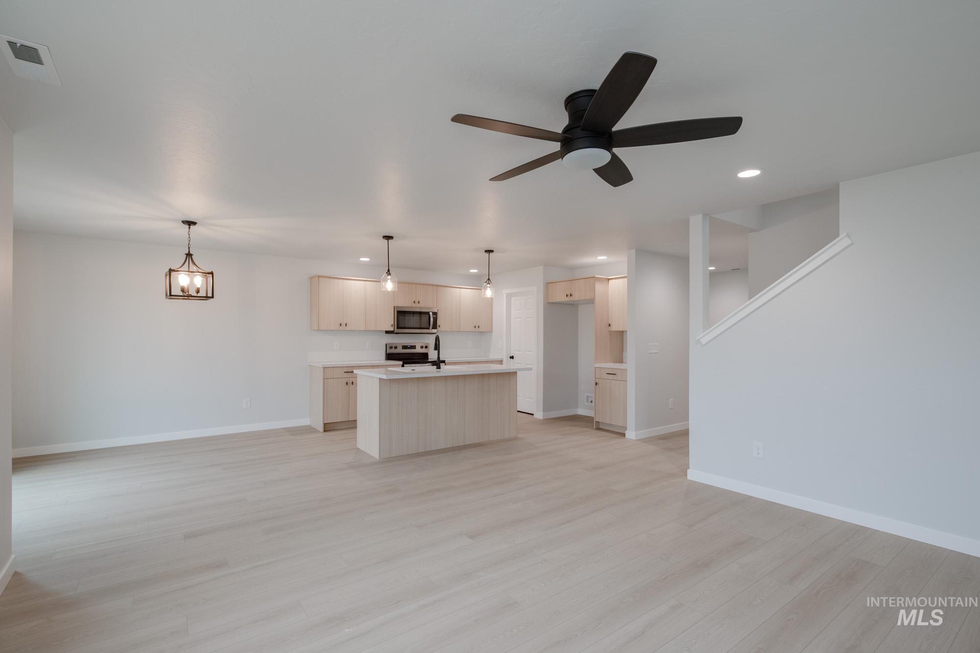 Kitchen featuring open floor plan, light countertops, a center island with sink, hanging light fixtures, and ceiling fan