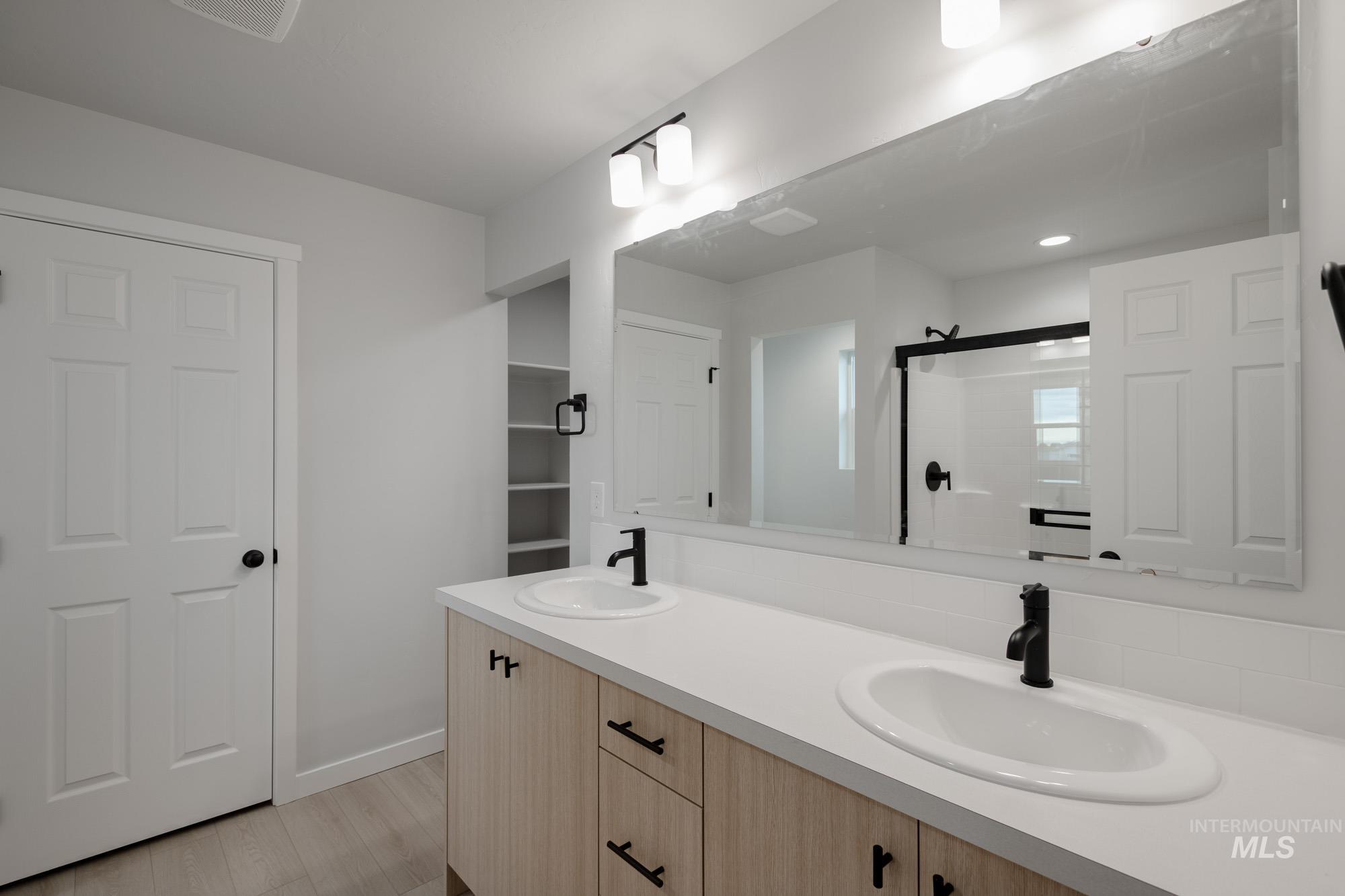 Full bathroom featuring a shower stall, double vanity, and light wood-style floors