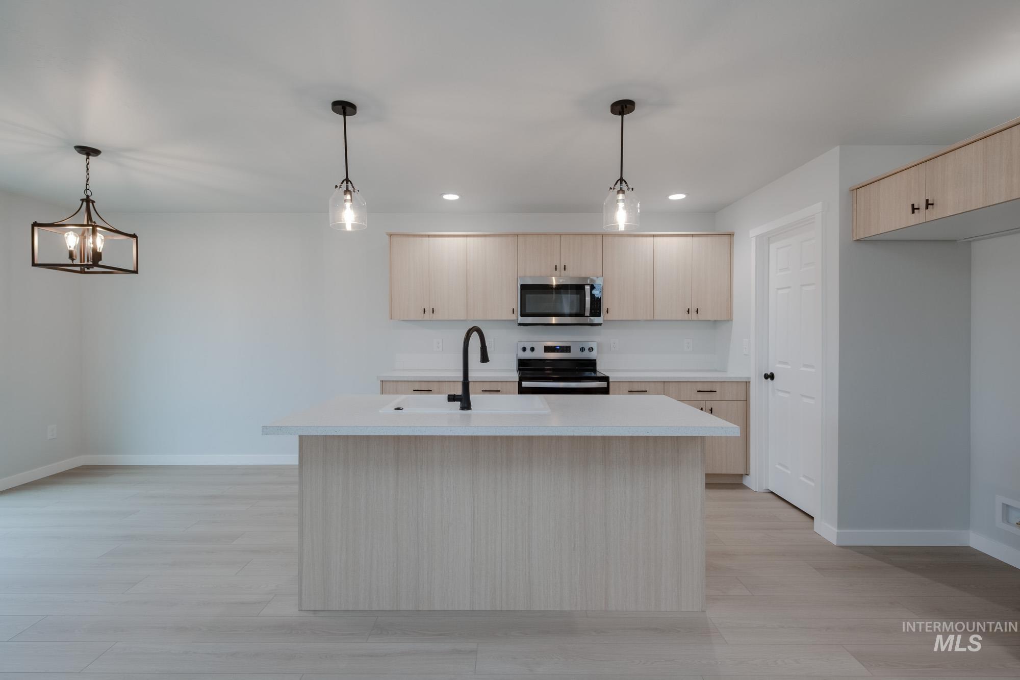 Kitchen with light countertops, hanging light fixtures, stainless steel appliances, light wood-type flooring, and light brown cabinetry