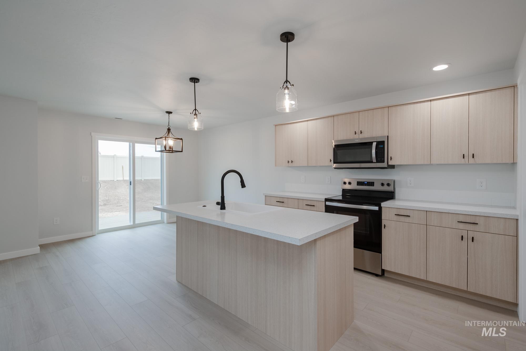 Kitchen featuring appliances with stainless steel finishes, light brown cabinets, light countertops, pendant lighting, and a kitchen island with sink