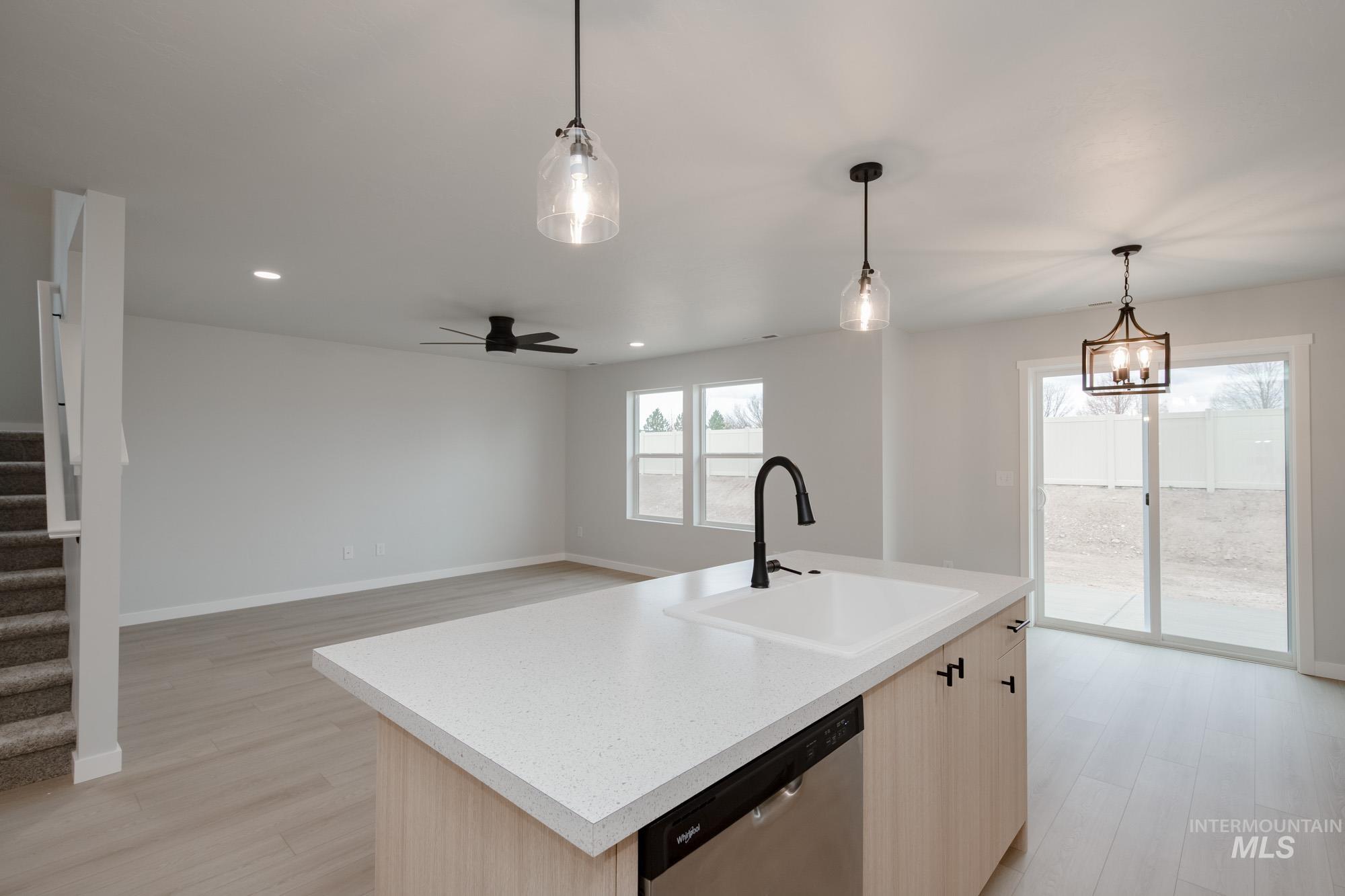 Kitchen with light brown cabinets, light wood-type flooring, hanging light fixtures, stainless steel dishwasher, and a kitchen island with sink