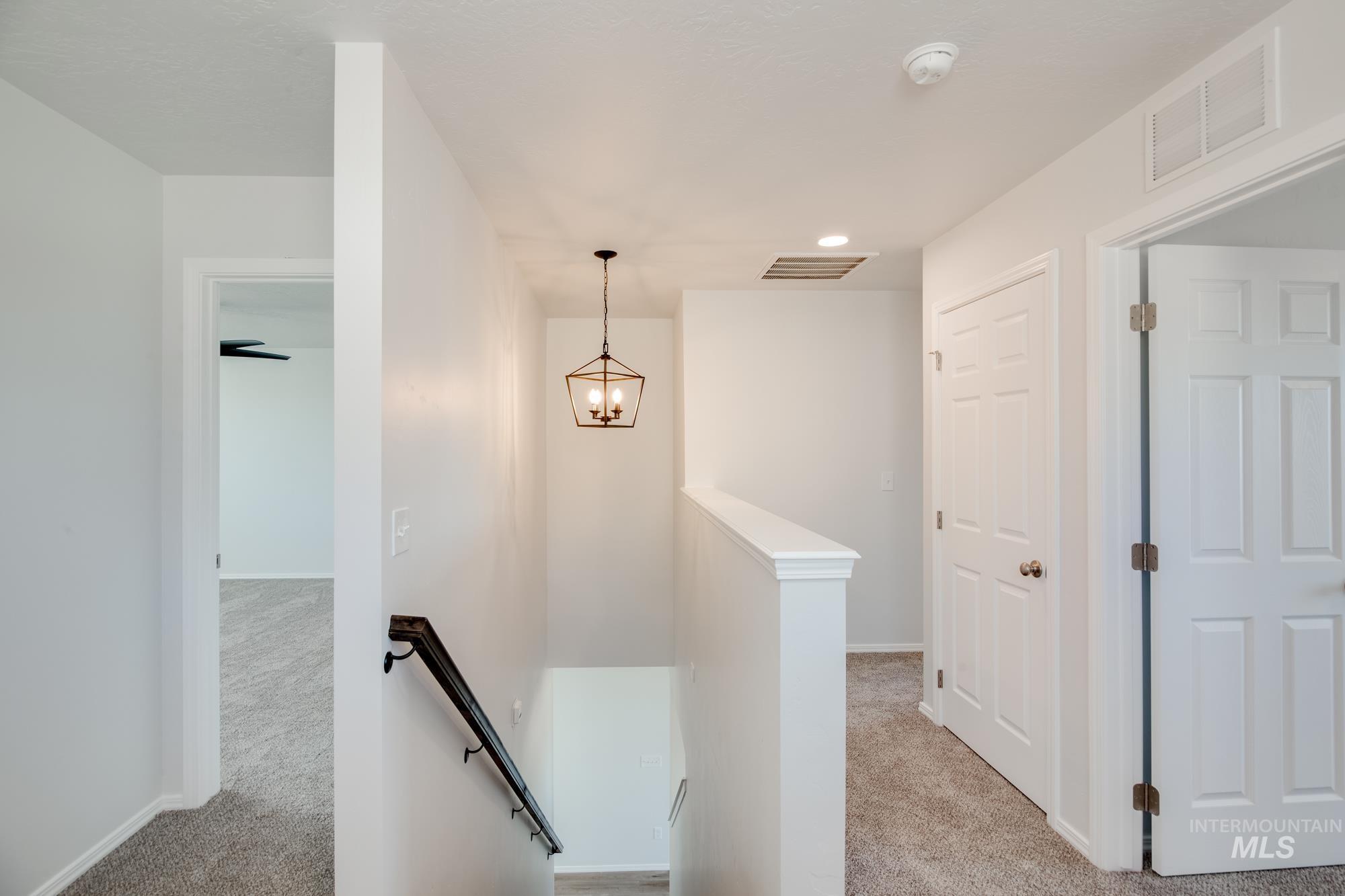 Hall featuring an upstairs landing, light colored carpet, and a chandelier