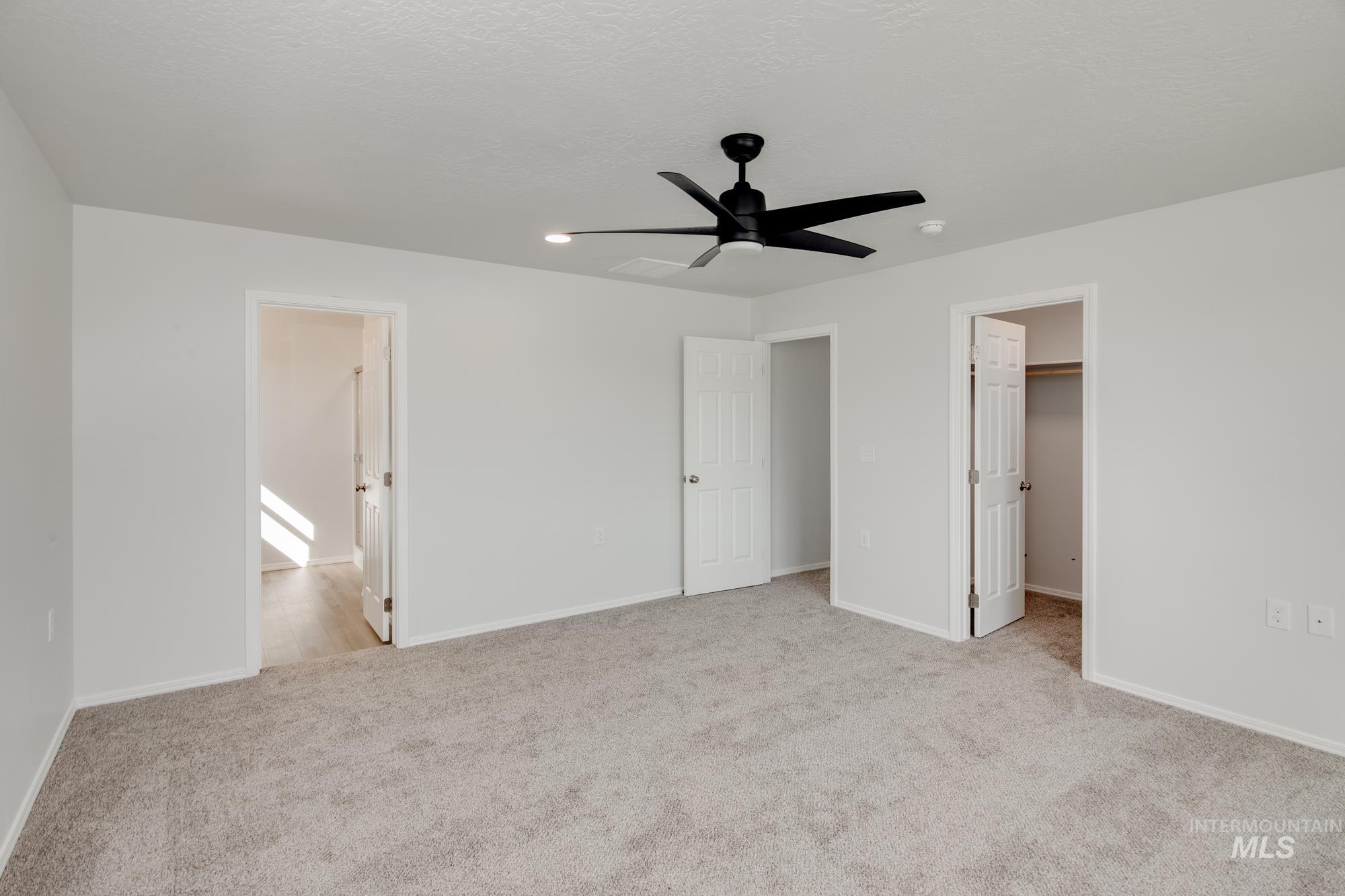 Unfurnished bedroom featuring a walk in closet, light carpet, ceiling fan, ensuite bath, and a textured ceiling