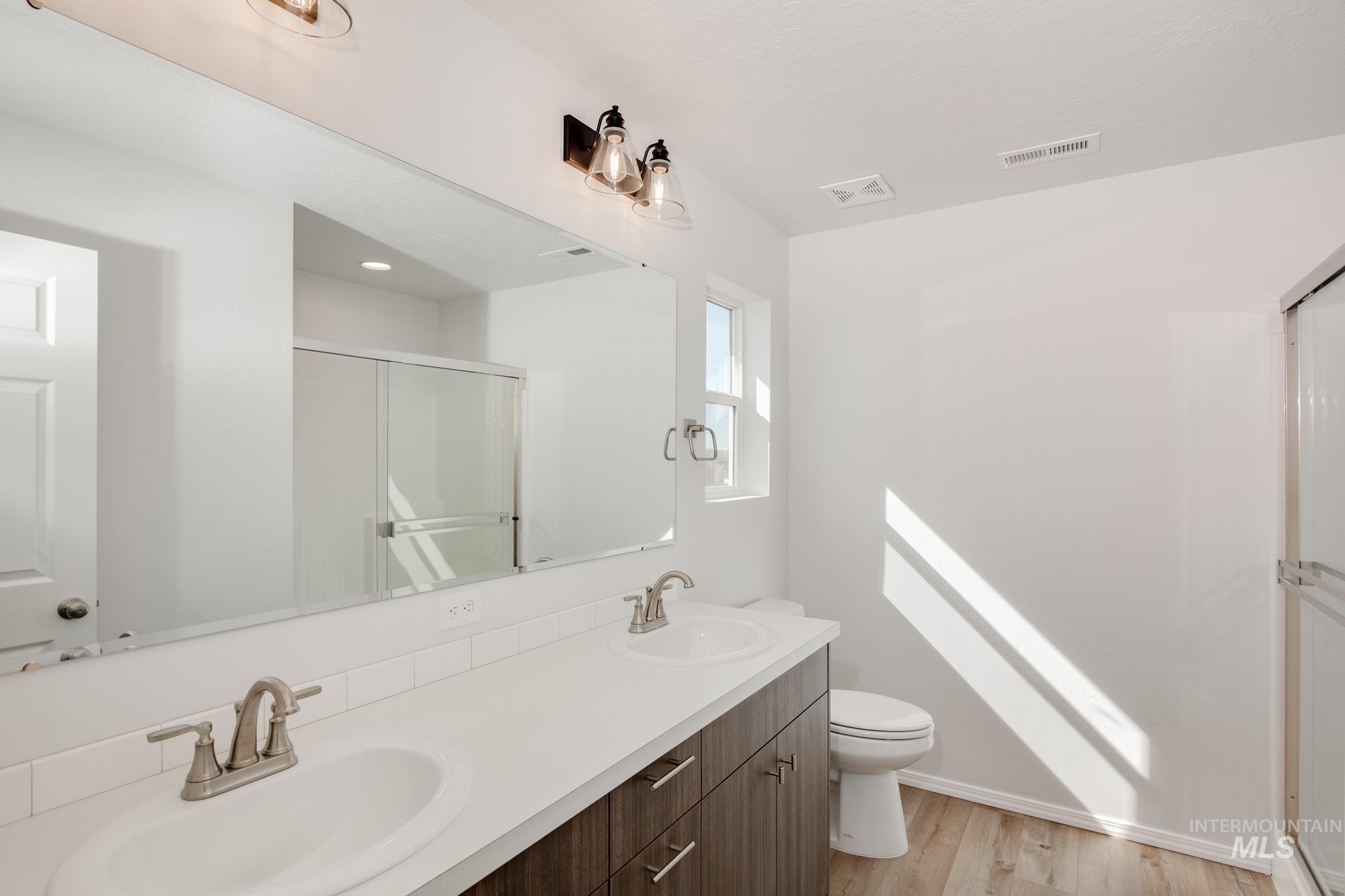Full bath featuring a shower stall, light wood finished floors, and double vanity
