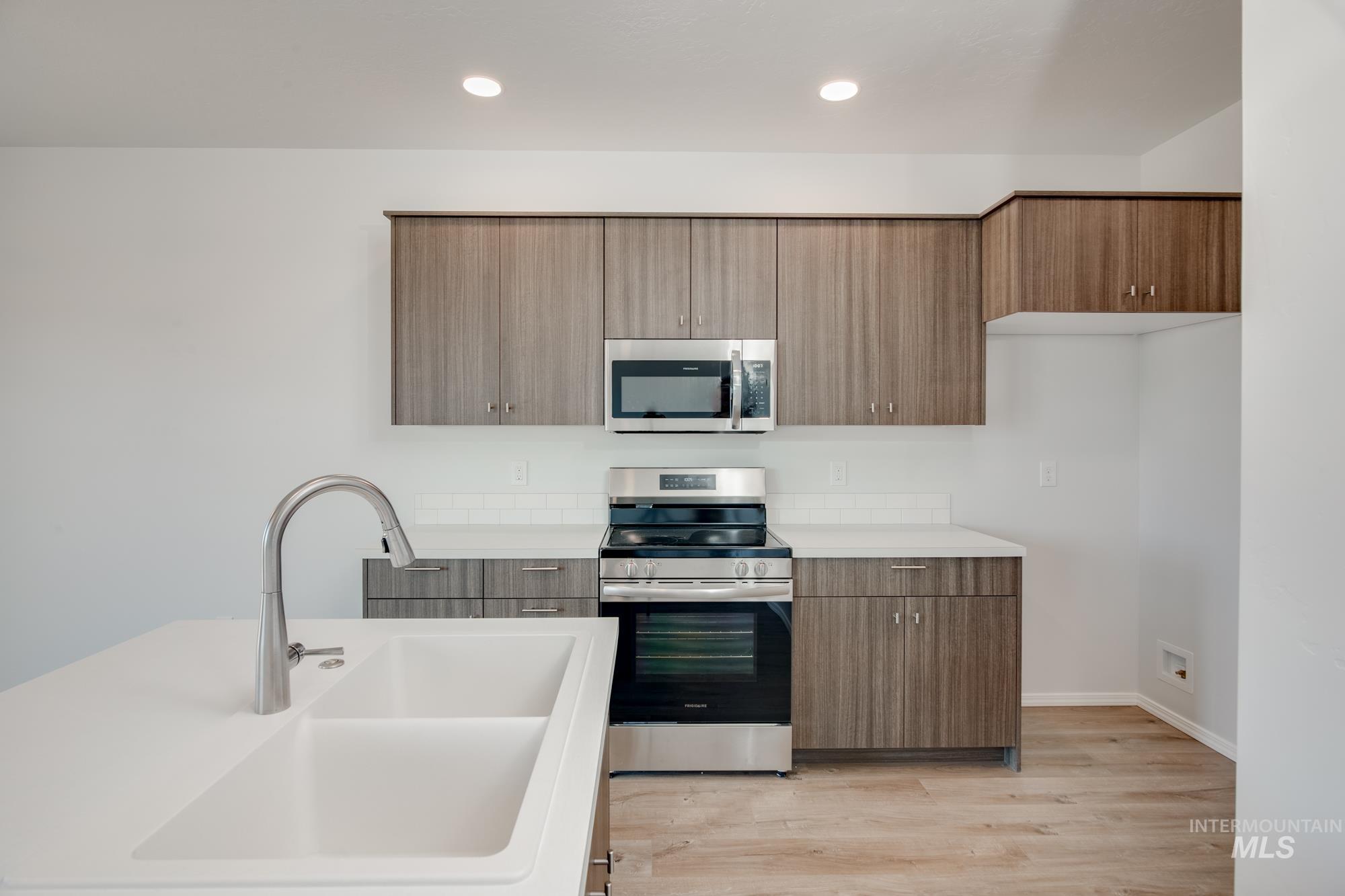 Kitchen with stainless steel appliances, light wood finished floors, modern cabinets, brown cabinets, and recessed lighting