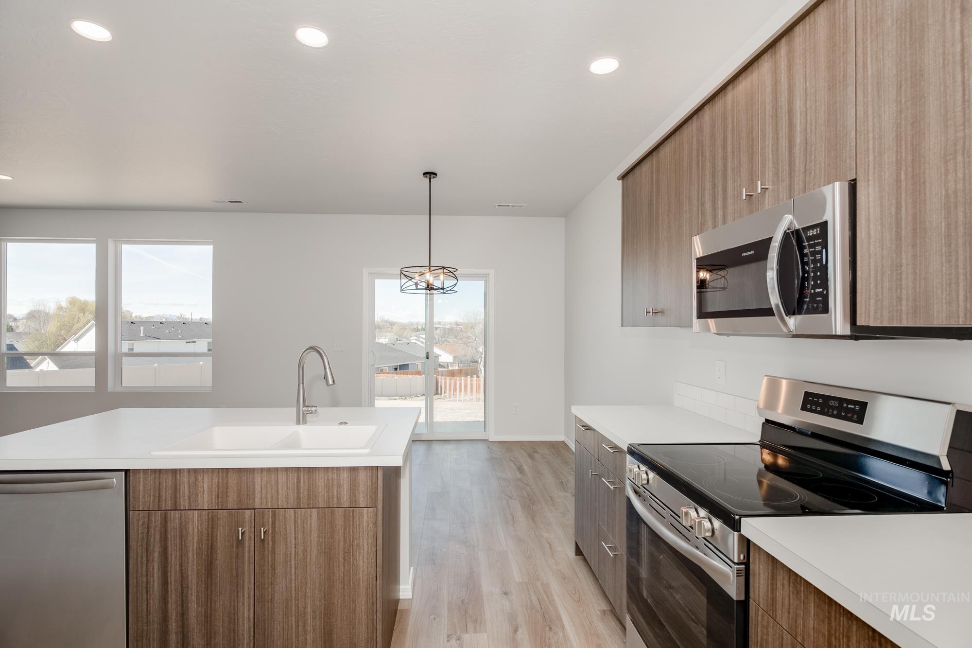 Kitchen featuring stainless steel appliances, hanging light fixtures, light countertops, light wood-style floors, and recessed lighting