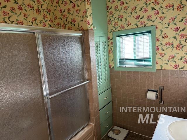Bathroom with a wainscoted wall, wallpapered walls, vanity, tile walls, and an enclosed shower