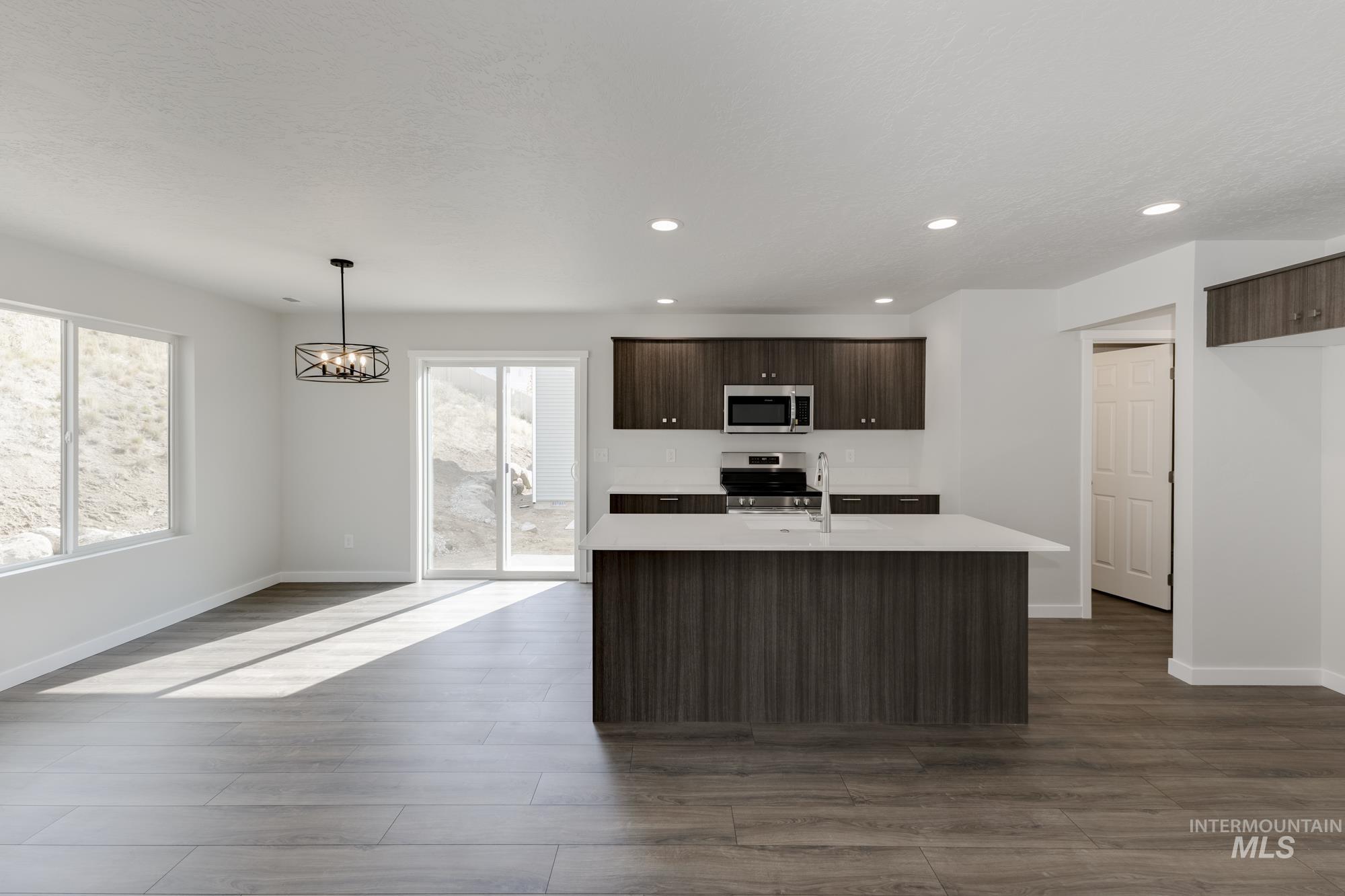 Kitchen with dark brown cabinetry, pendant lighting, a center island with sink, dark wood-style floors, and appliances with stainless steel finishes