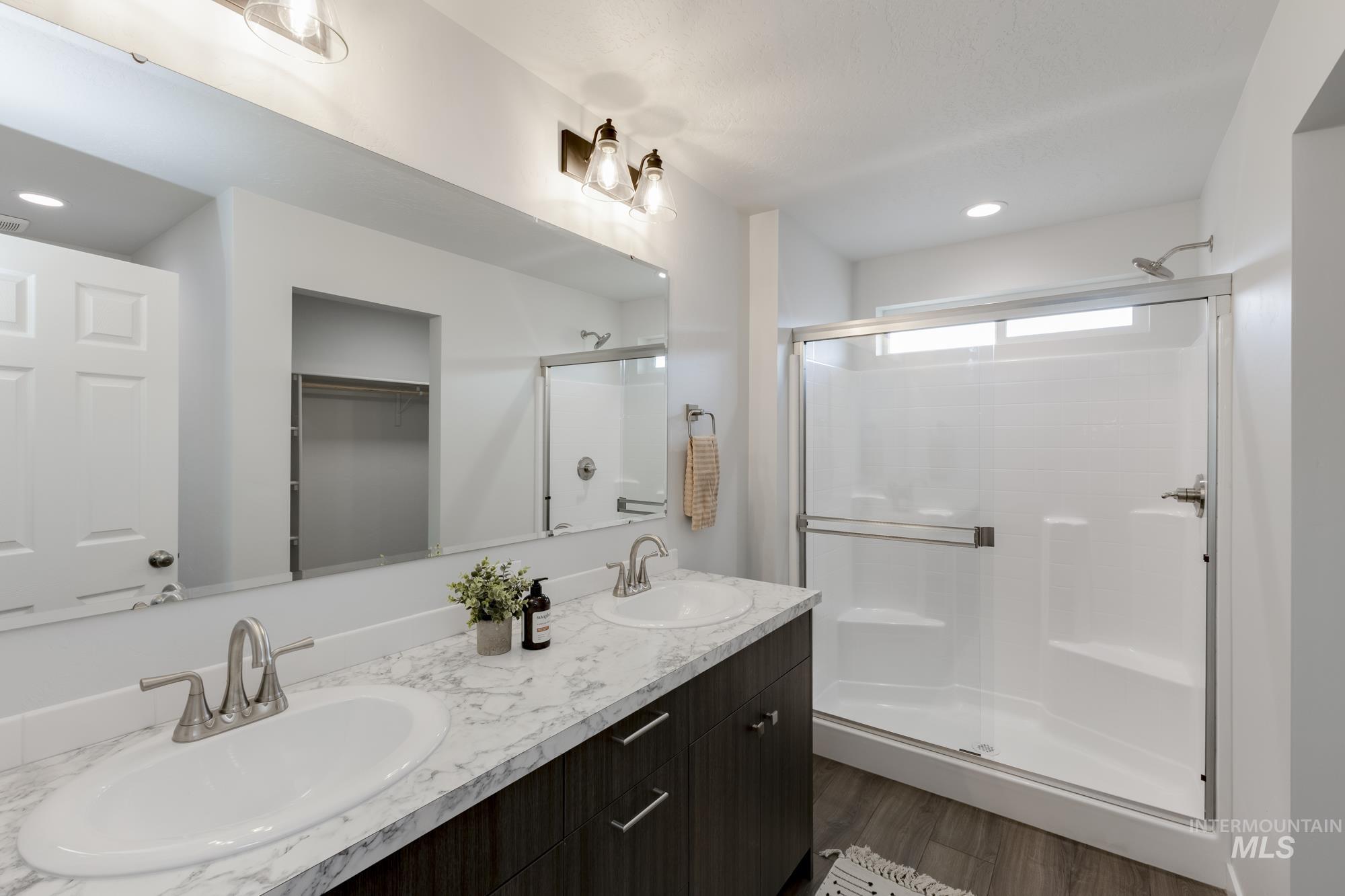 Bathroom with dark wood-style floors, double vanity, a walk in closet, recessed lighting, and a stall shower