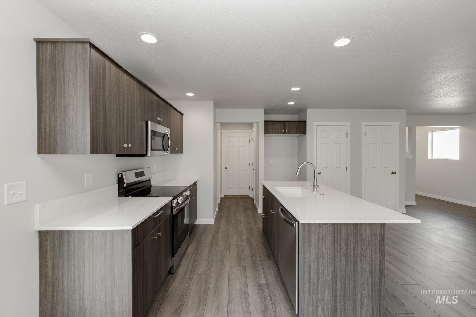 Kitchen featuring appliances with stainless steel finishes, modern cabinets, a kitchen island with sink, light wood finished floors, and dark brown cabinetry