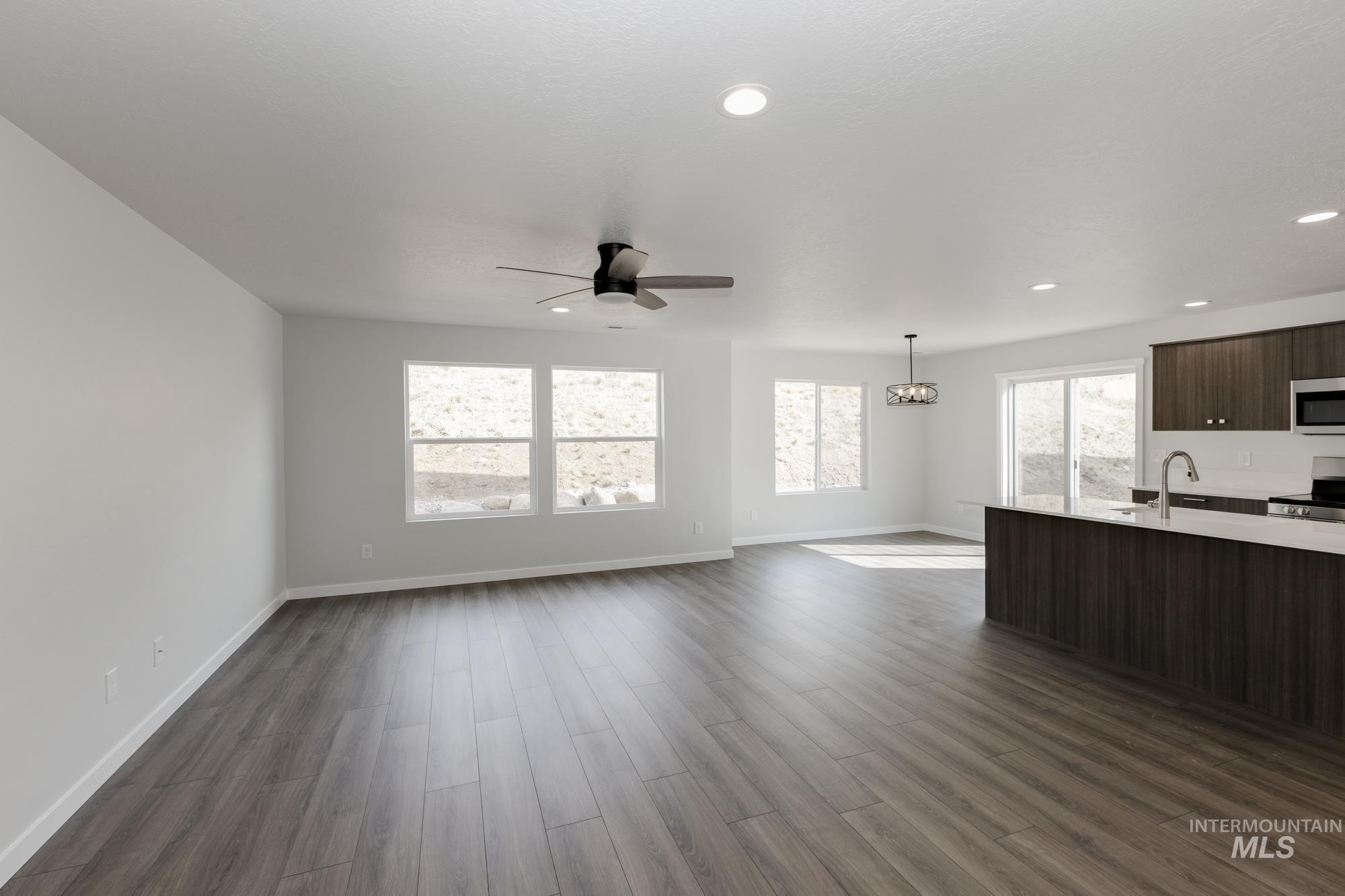 Unfurnished living room featuring dark wood finished floors, a ceiling fan, recessed lighting, and a chandelier