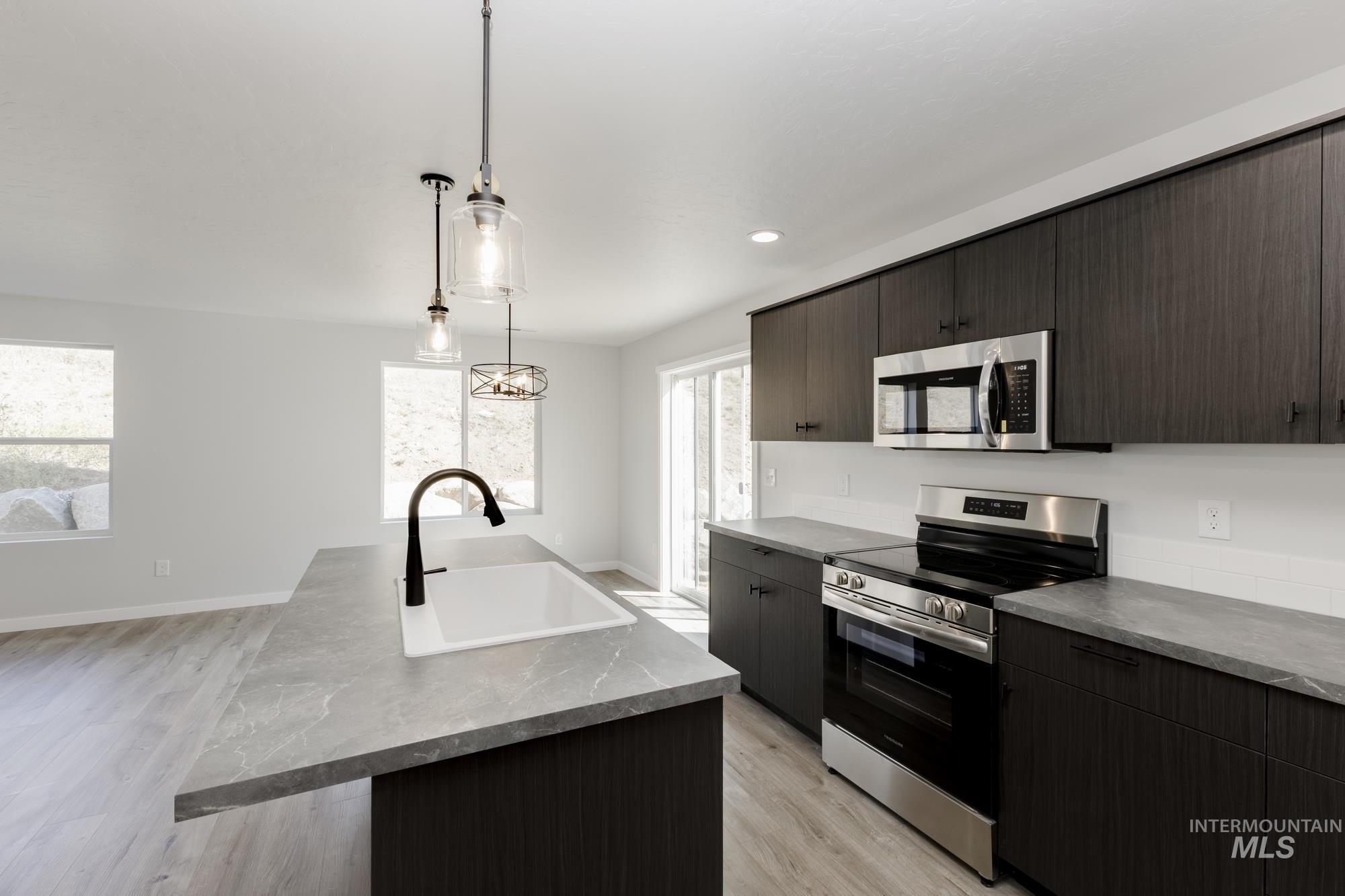 Kitchen with stainless steel appliances, light wood-style flooring, decorative light fixtures, a center island with sink, and modern cabinets